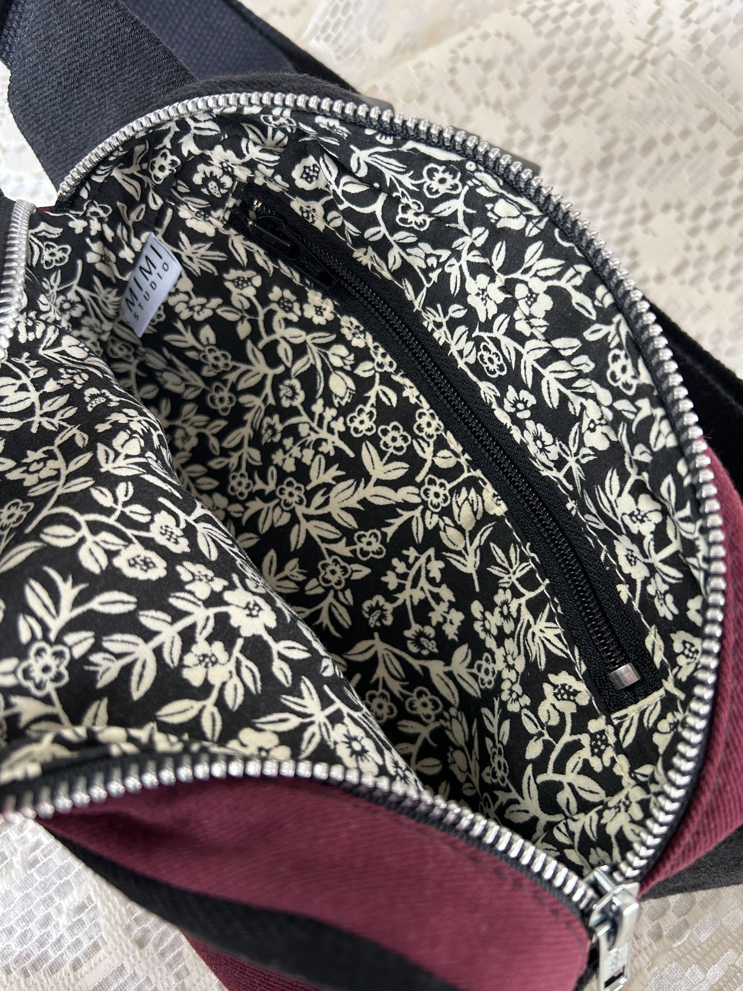 Interior black and ivory floral patterned lining of the fanny pack with a zippered pocket