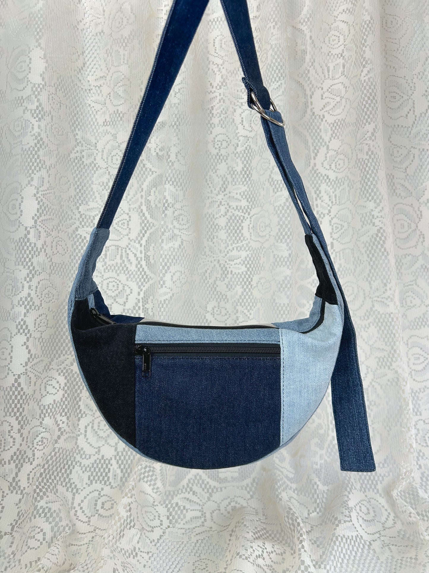 Multi-coloured denim crescent bag with a zippered pocket in front of a white lace backdrop