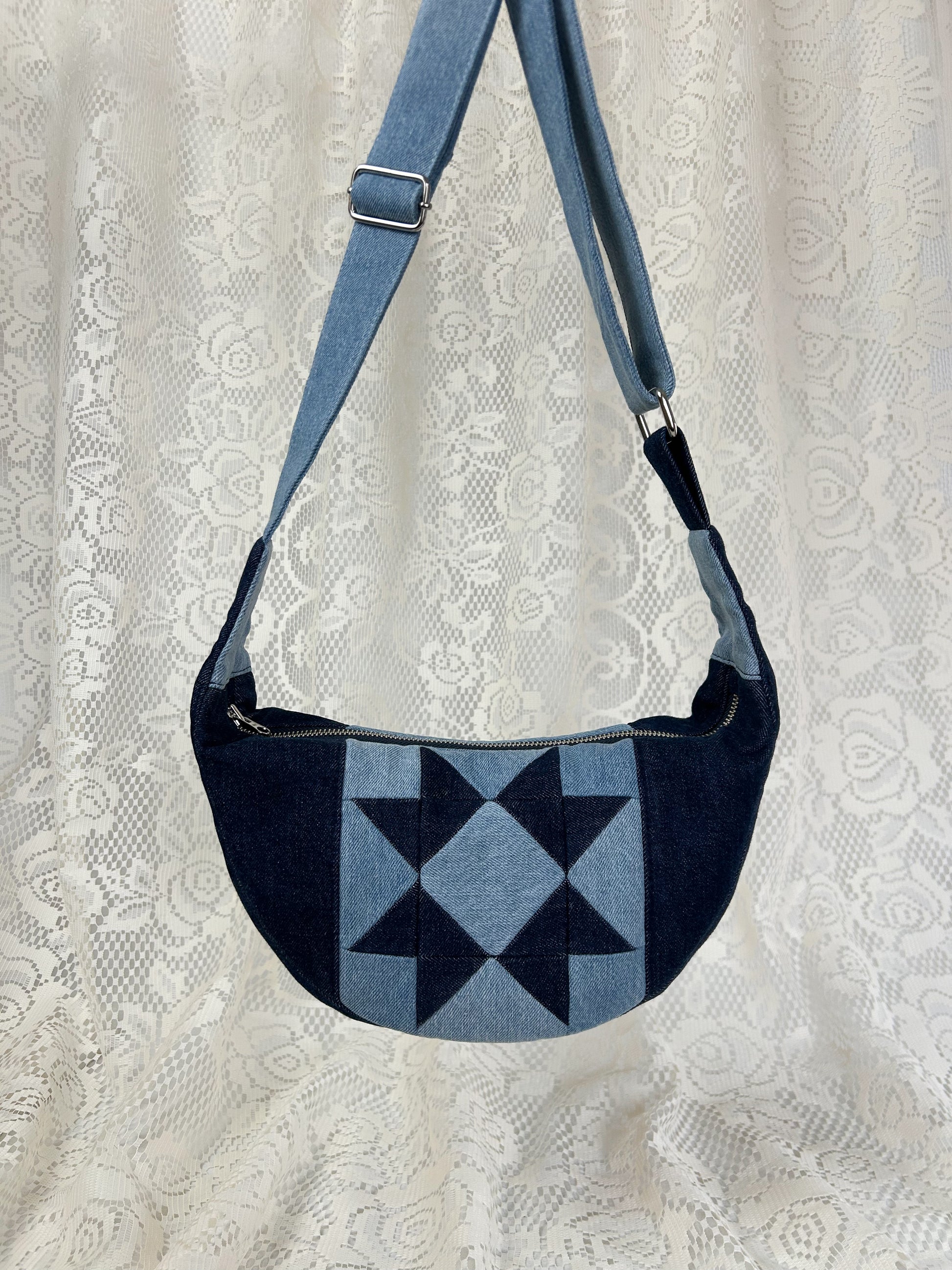 Two tone blue denim crescent bag with a patchwork star pattern in front of a white lace backdrop