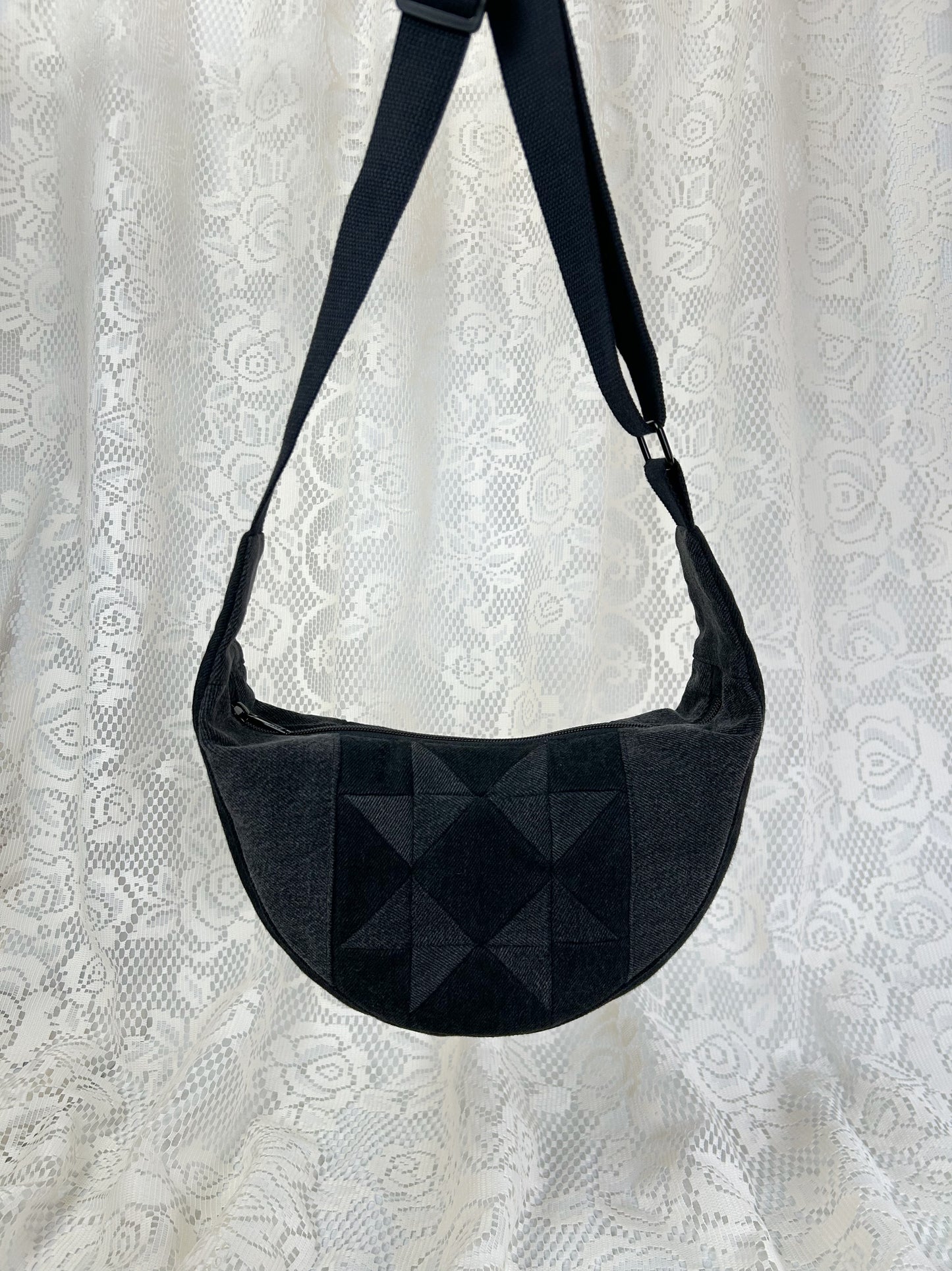 Black and grey denim crescent bag with a patchwork star pattern in front of a white lace backdrop.