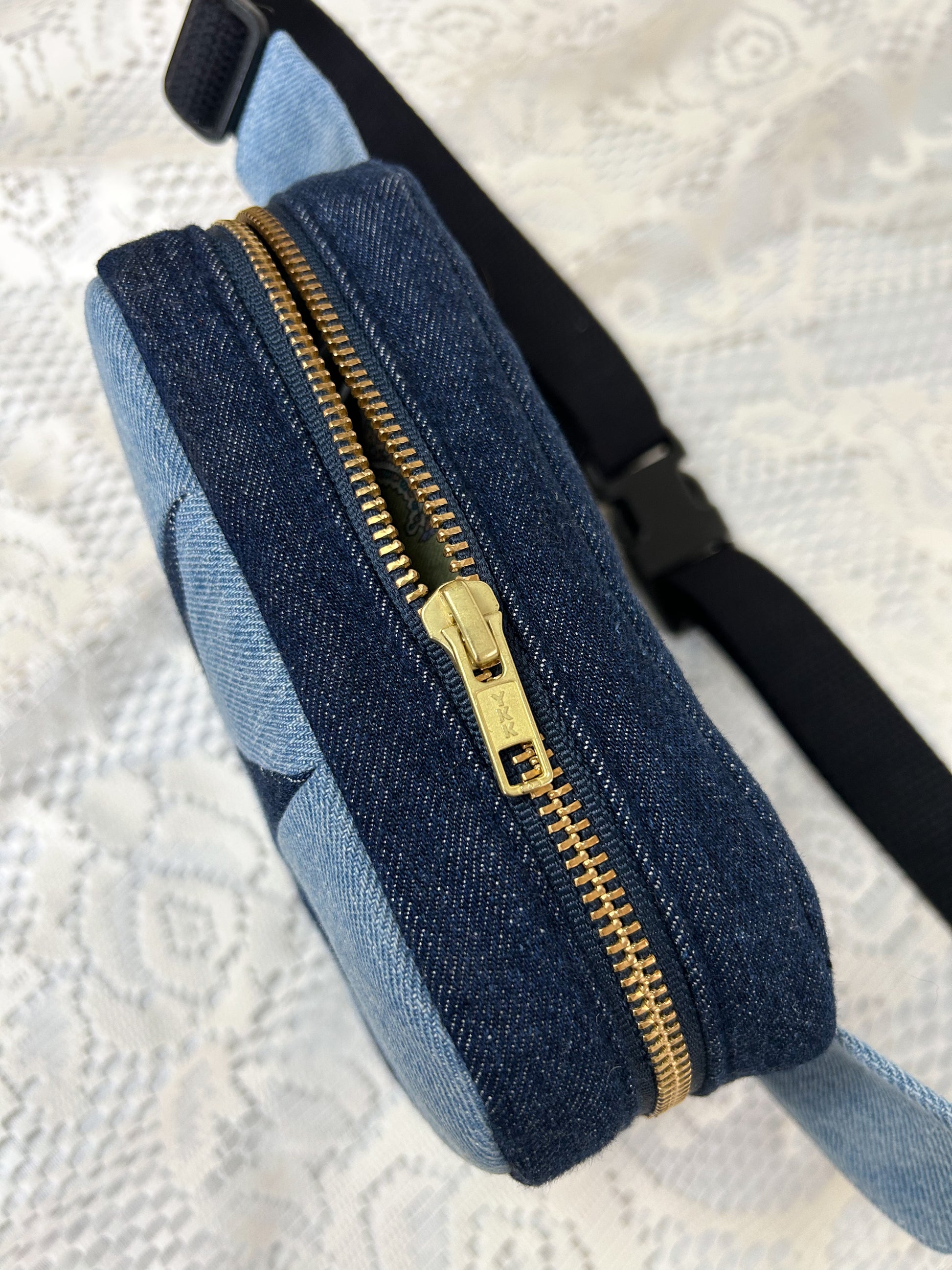 Top view of the two tone blue denim fanny pack with a patchwork star pattern showing the brass zipper on a white lace background
