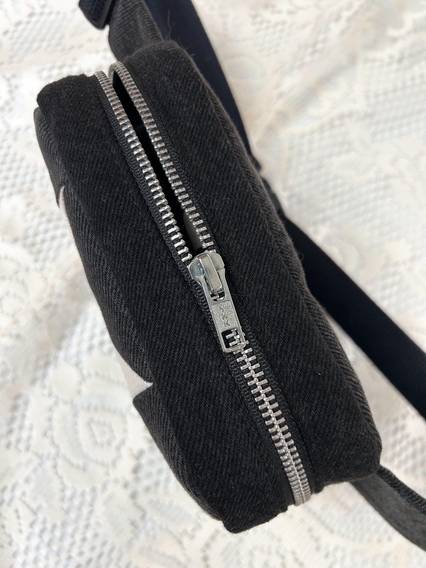 Top view of the grey, black and ivory denim fanny pack with a patchwork star pattern showing the aluminum zipper on a white lace background