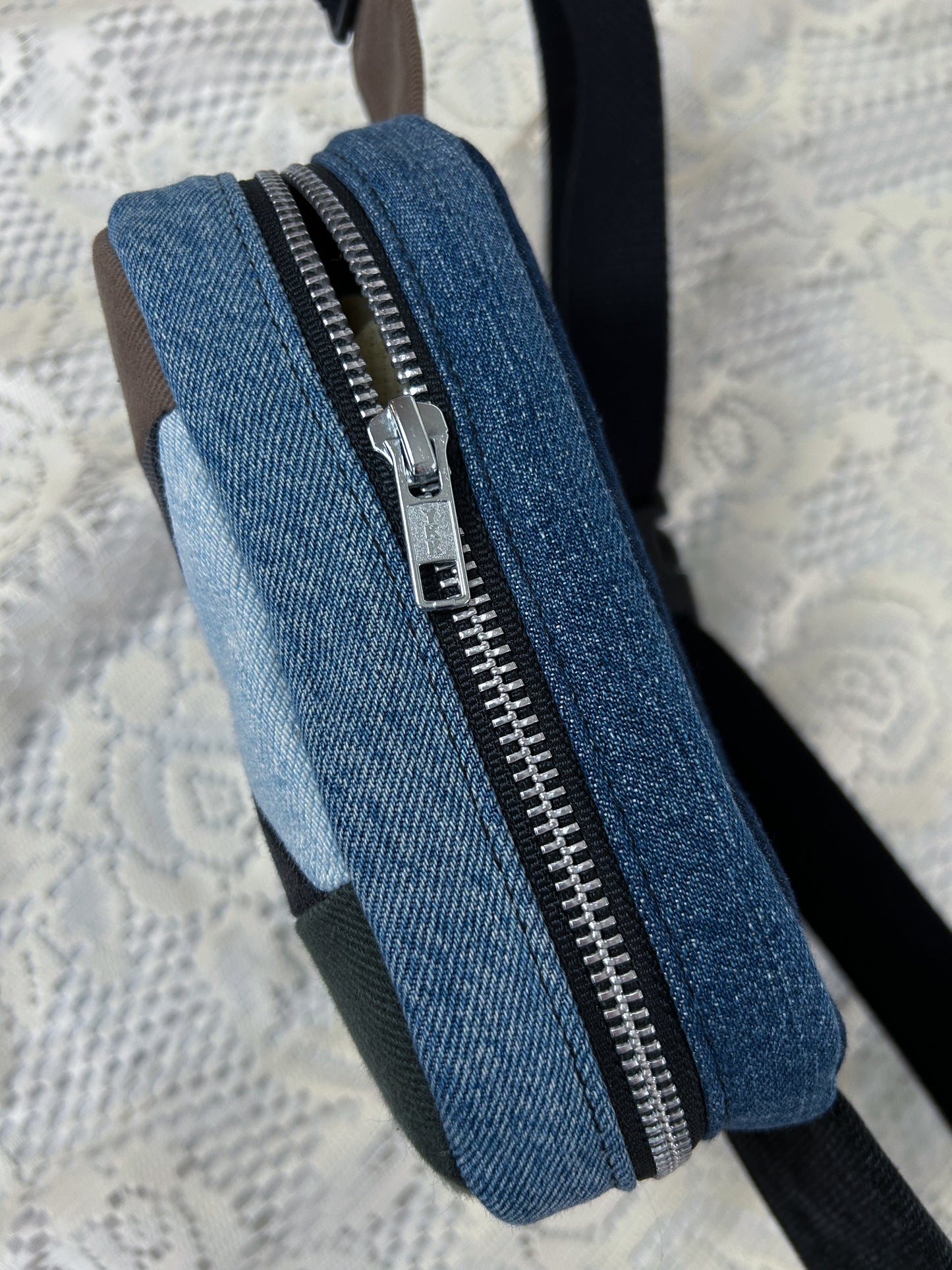 Top view of the multi-coloured denim fanny pack with a patchwork star pattern showing the aluminum zipper on a white lace background