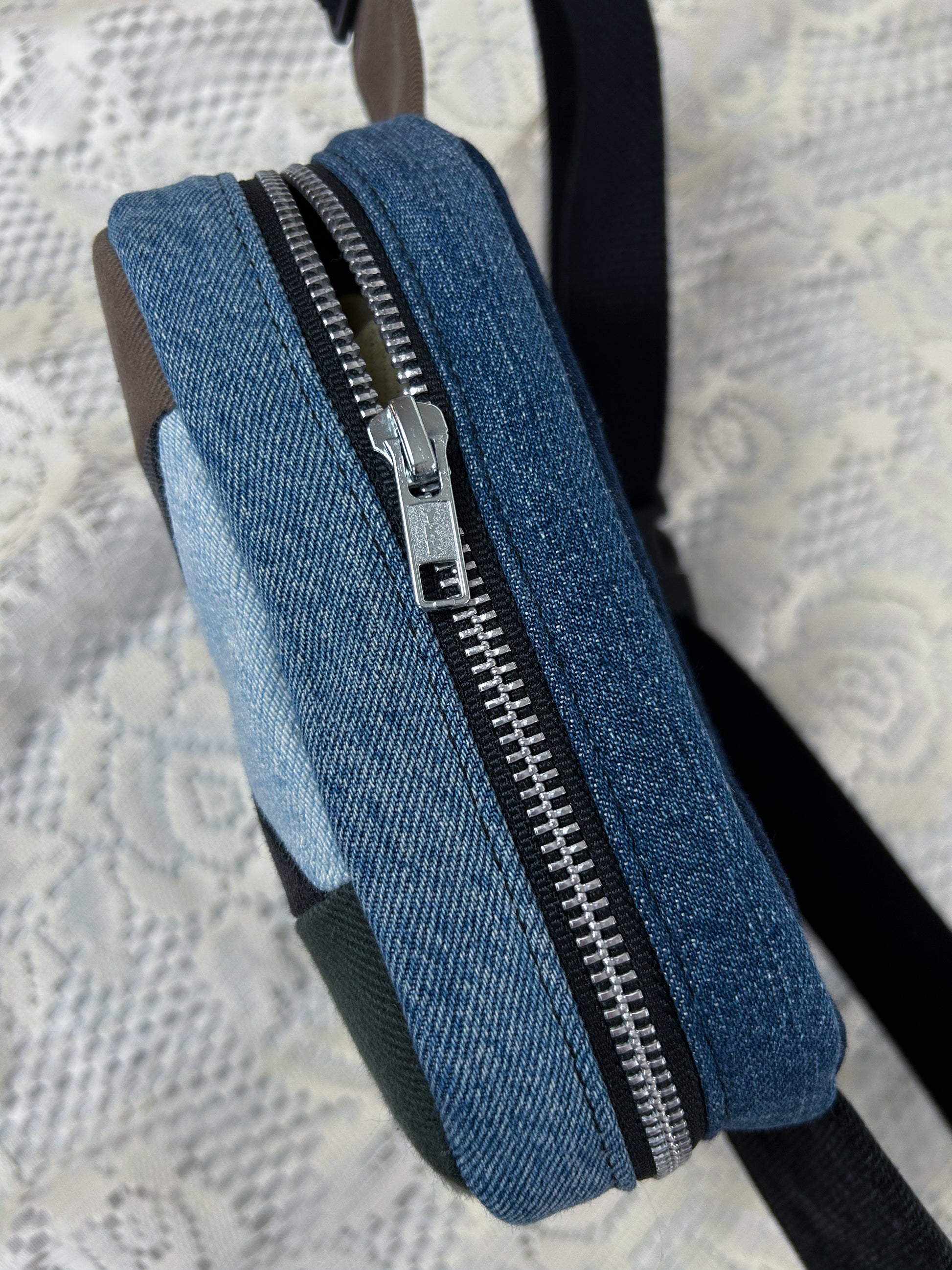Top view of the multi-coloured denim fanny pack with a patchwork star pattern showing the aluminum zipper on a white lace background