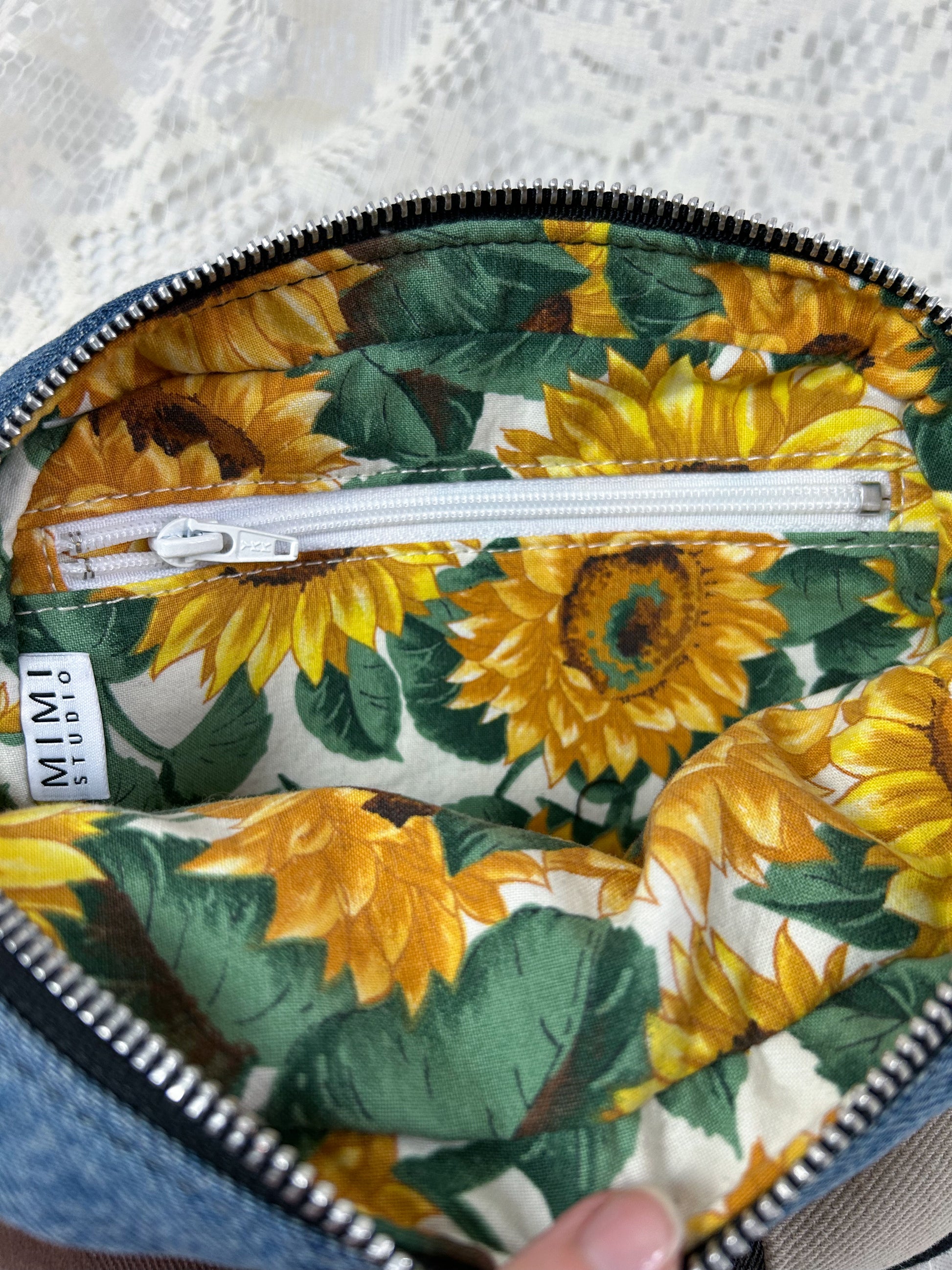 Close up of the lining for the multi-coloured denim fanny pack which is cotton fabric with a sunflower pattern and has a zippered pocket.