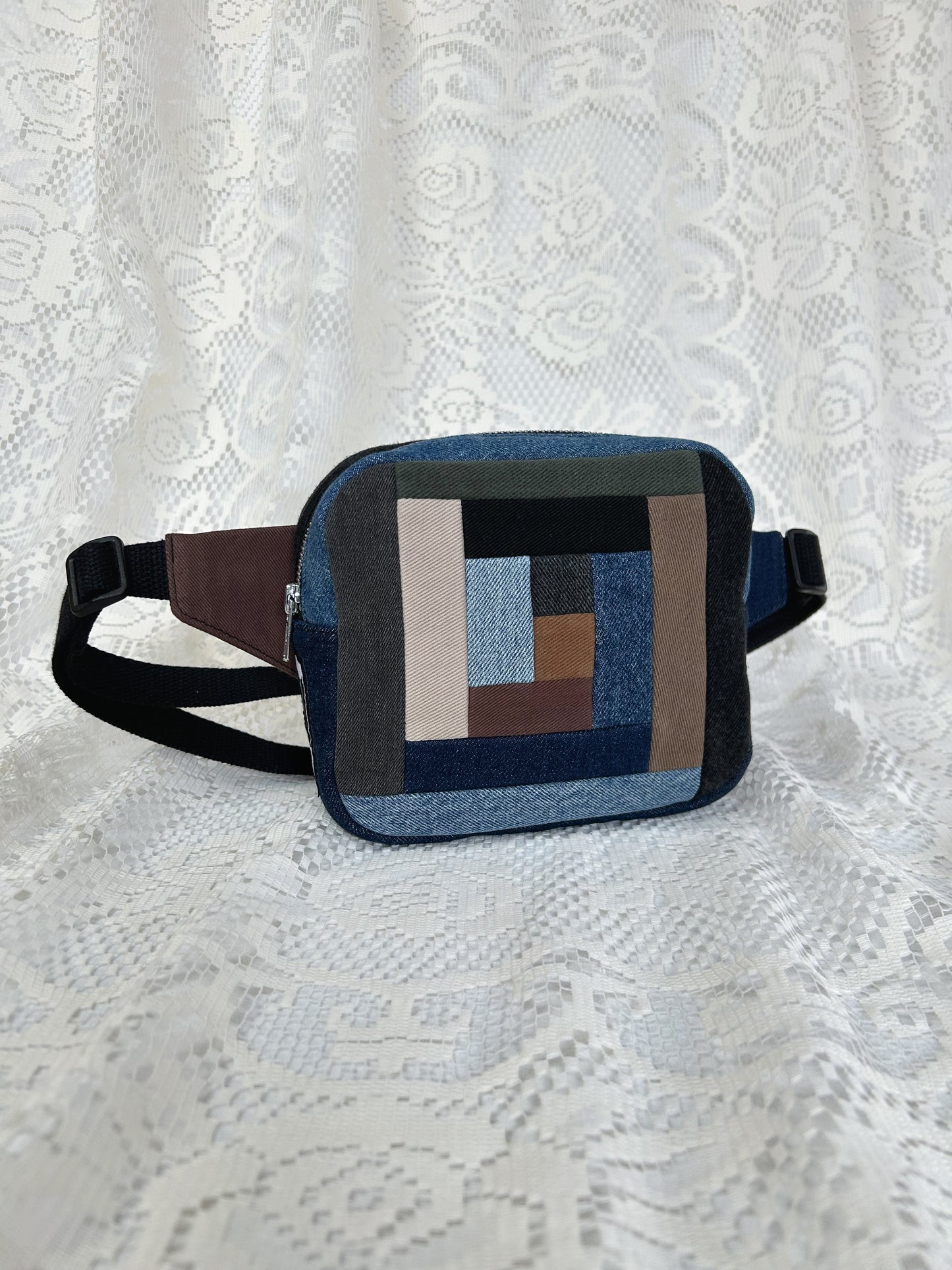 Fanny pack with a traditional log cabin patchwork design made using different colours and types of denim on a white lace background