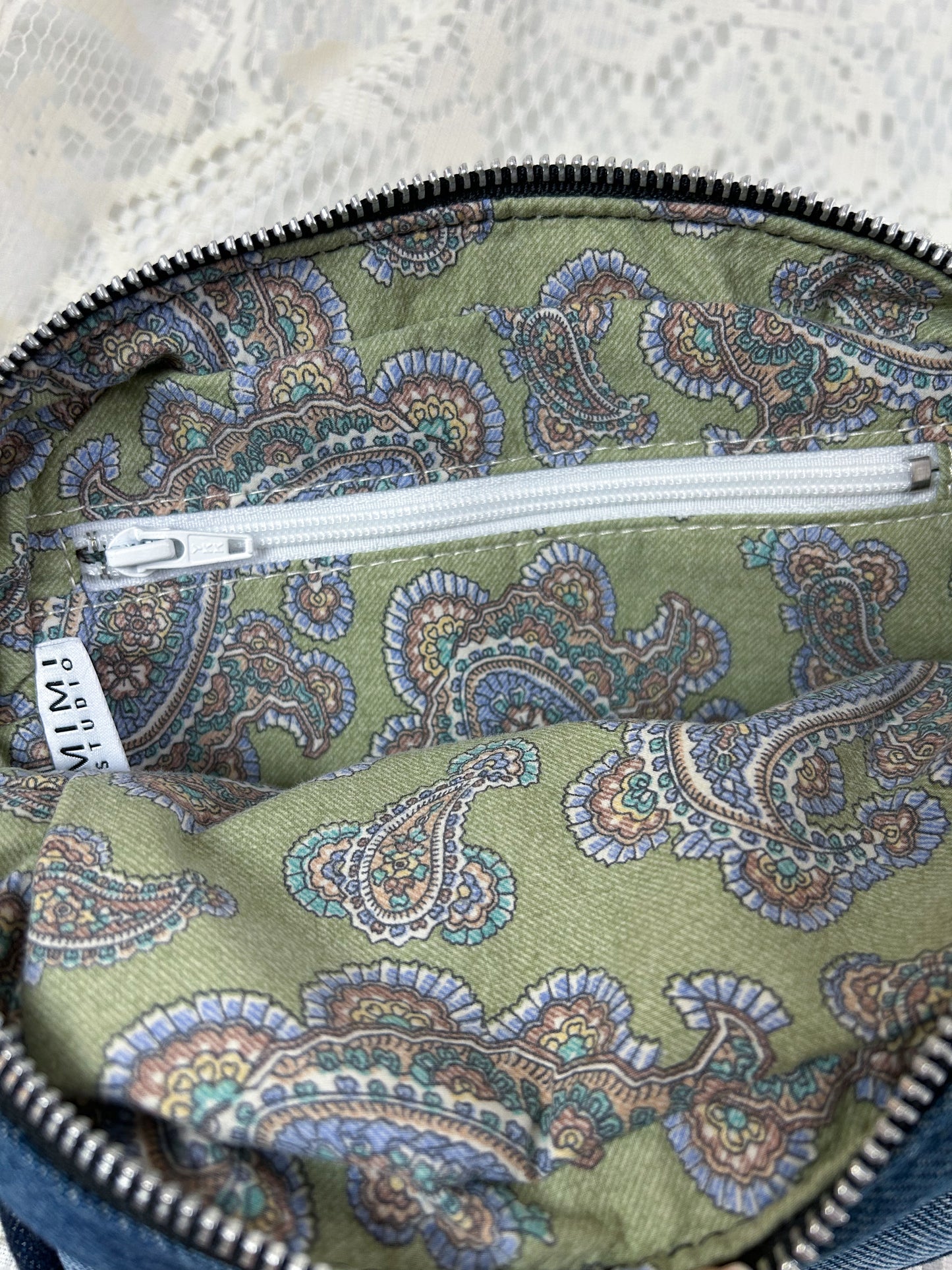 Lining fabric for the log cabin patchwork fanny pack which is paisley patterned cotton and has a zippered pocket on a white lace background