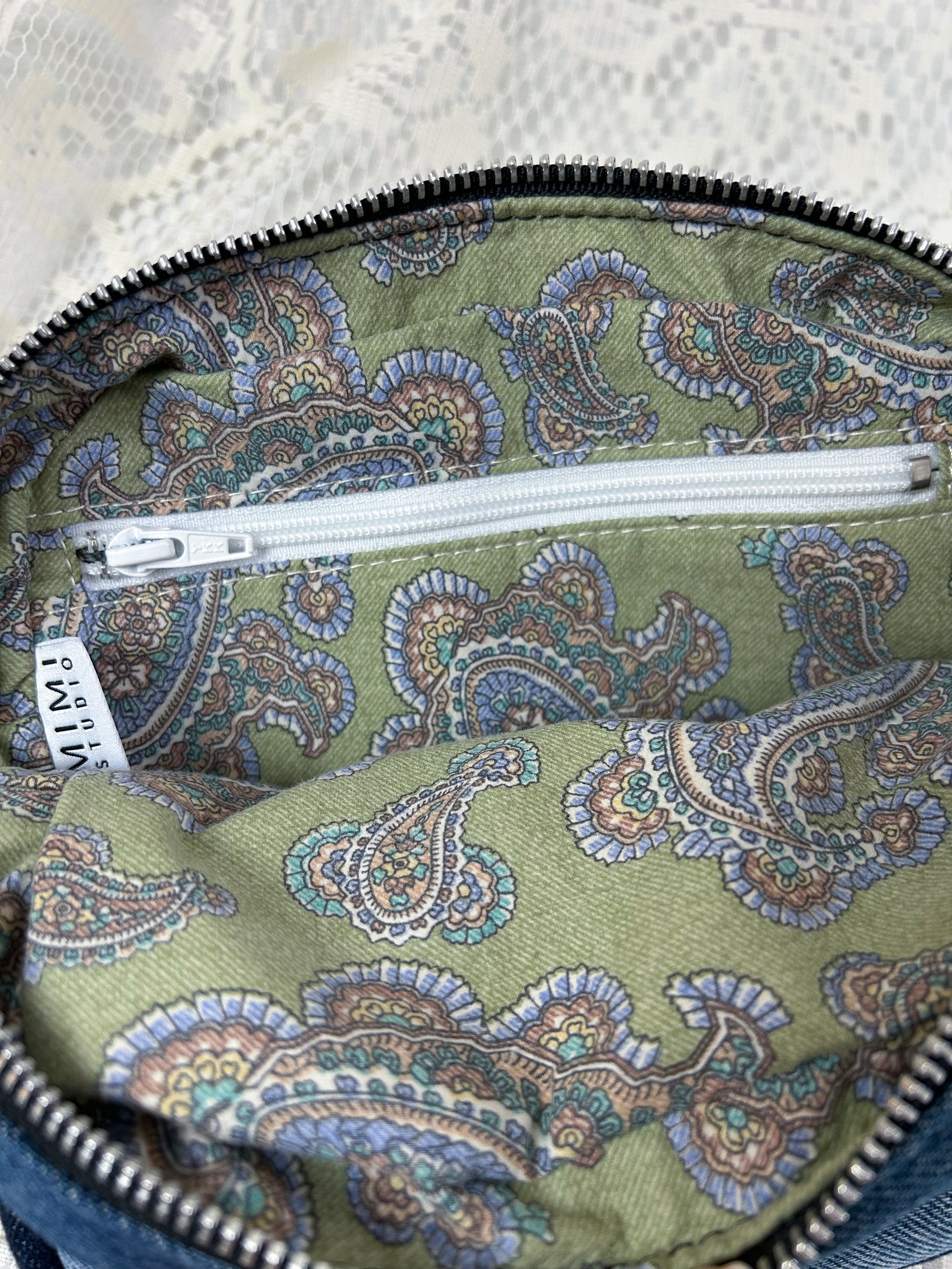 Lining fabric for the log cabin patchwork fanny pack which is paisley patterned cotton and has a zippered pocket on a white lace background