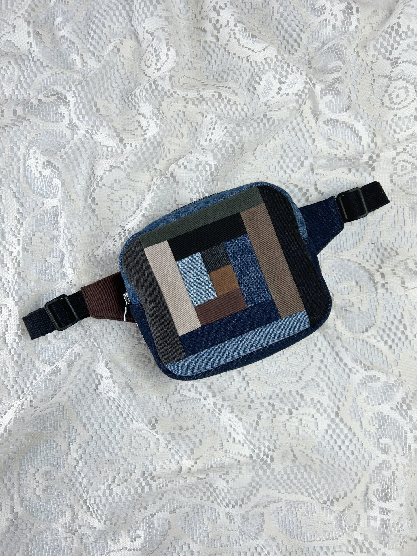 Fanny pack with a traditional log cabin patchwork design made using different colours and types of denim on a white lace background