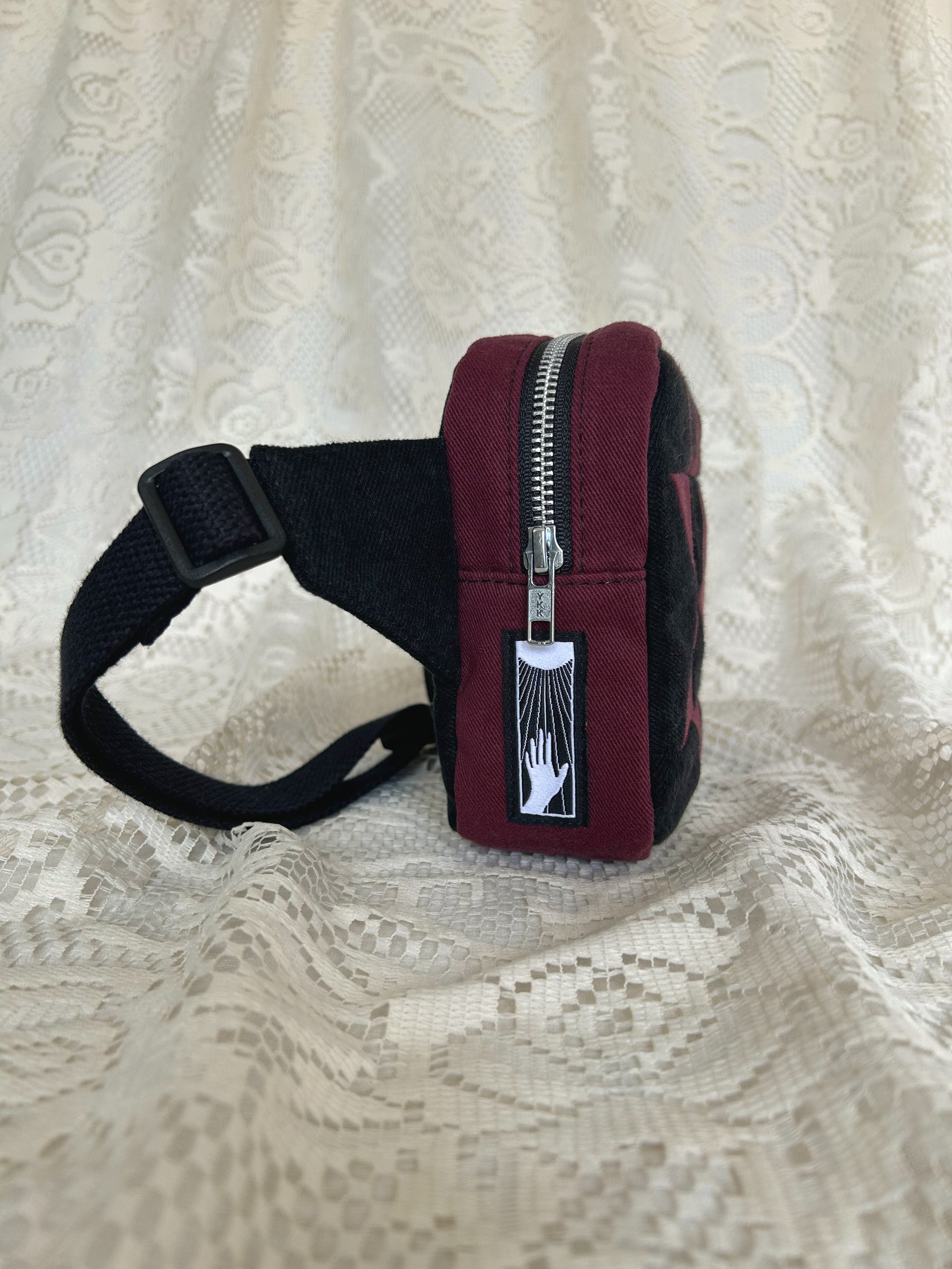 Side view of the same fanny pack showing the aluminum zipper and black cotton webbing strap with an ivory lace backdrop