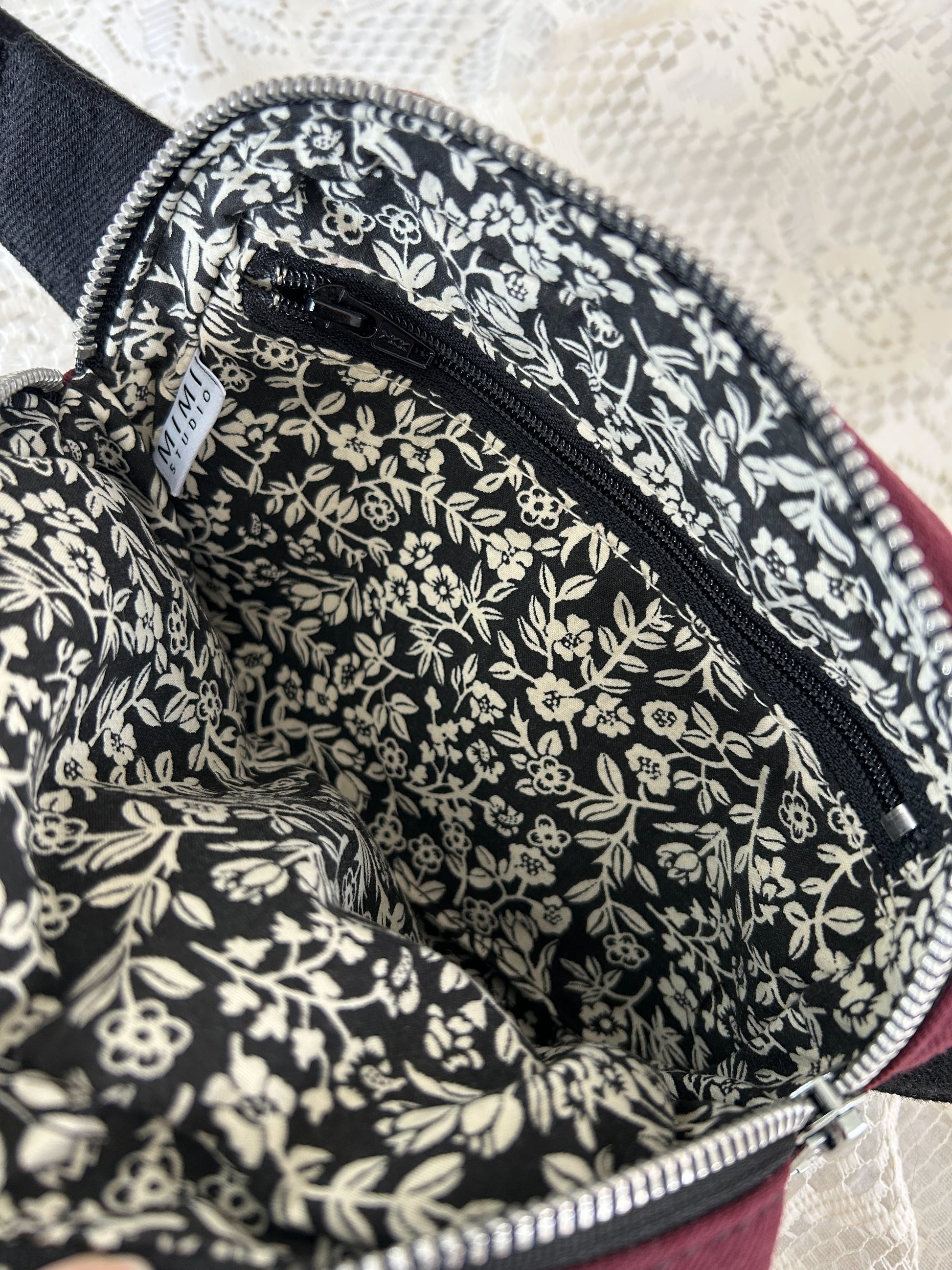 Black and ivory floral patterned interior lining of the fanny pack with a zippered pocket