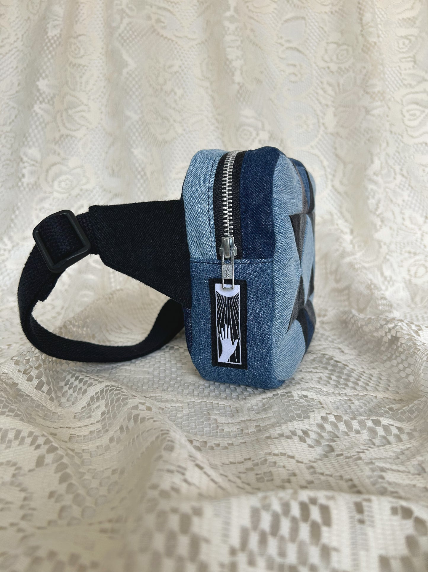 Side view of the same fanny pack showing the aluminum zipper and black cotton webbing strap with an ivory lace backdrop