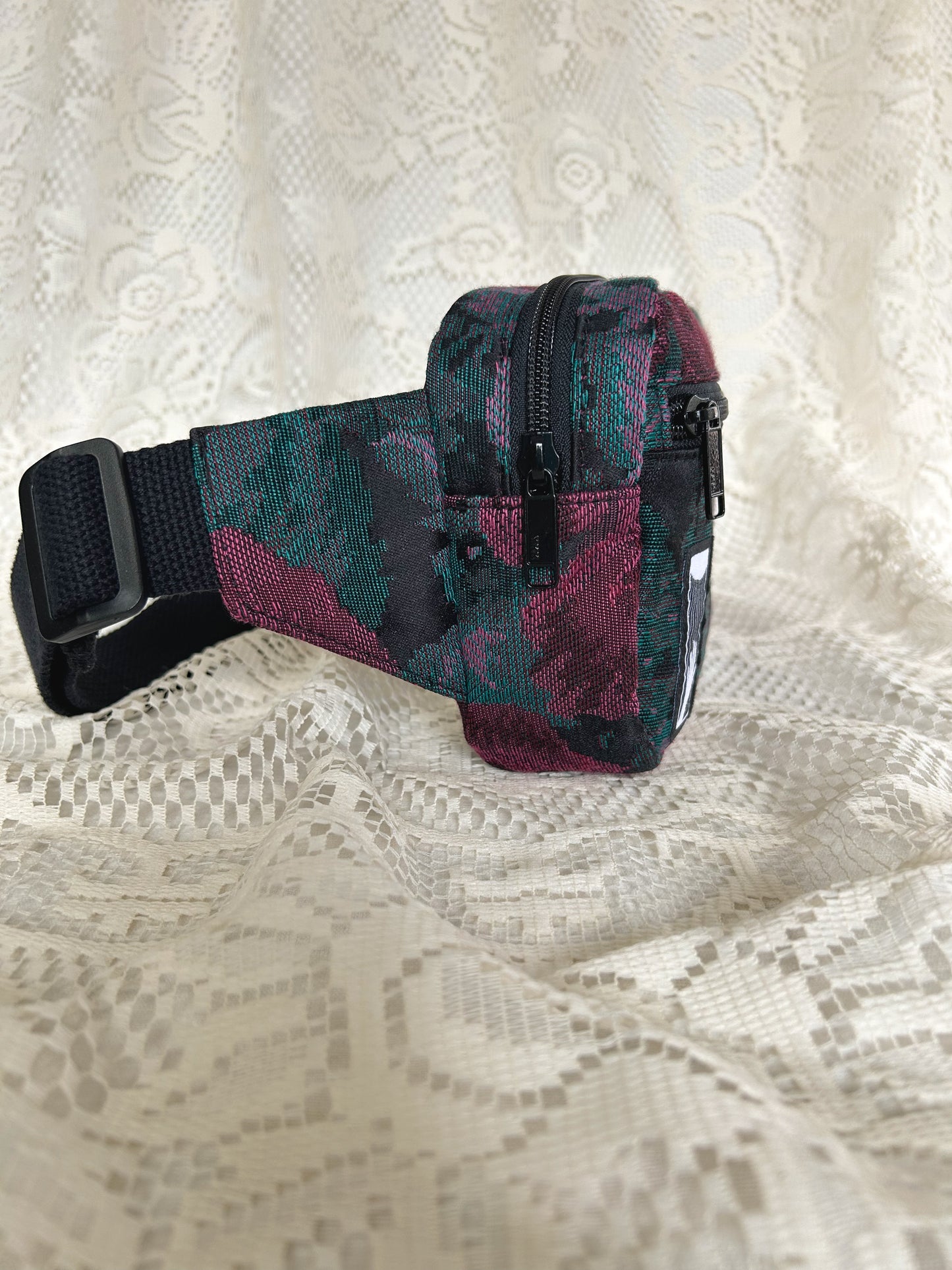 Side view of the black, burgundy, and turquoise floral patterned upholstery fabric fanny pack with an ivory lace backdrop