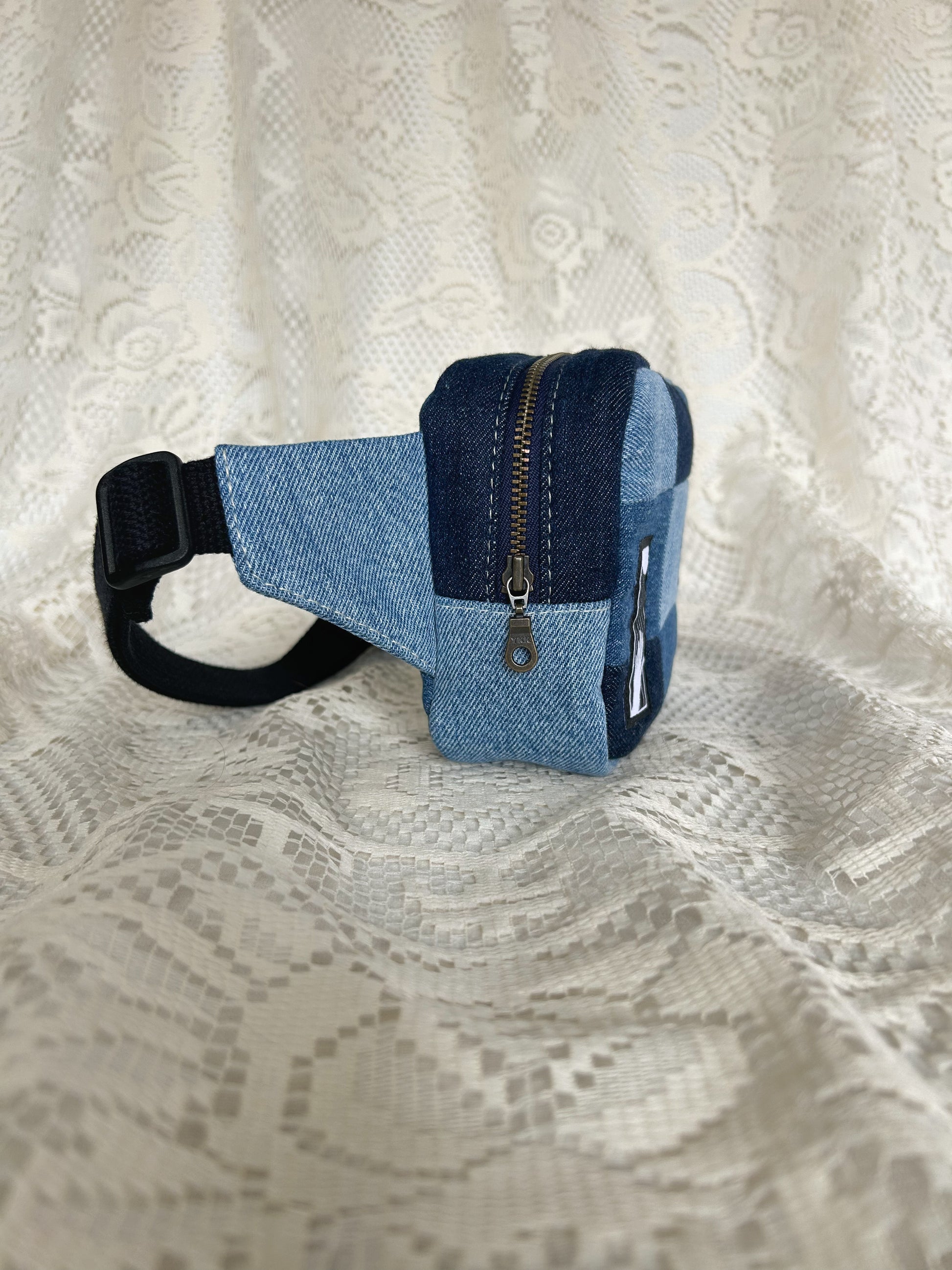 Side view of the same fanny pack showing the antique brass zipper with an ivory lace backdrop