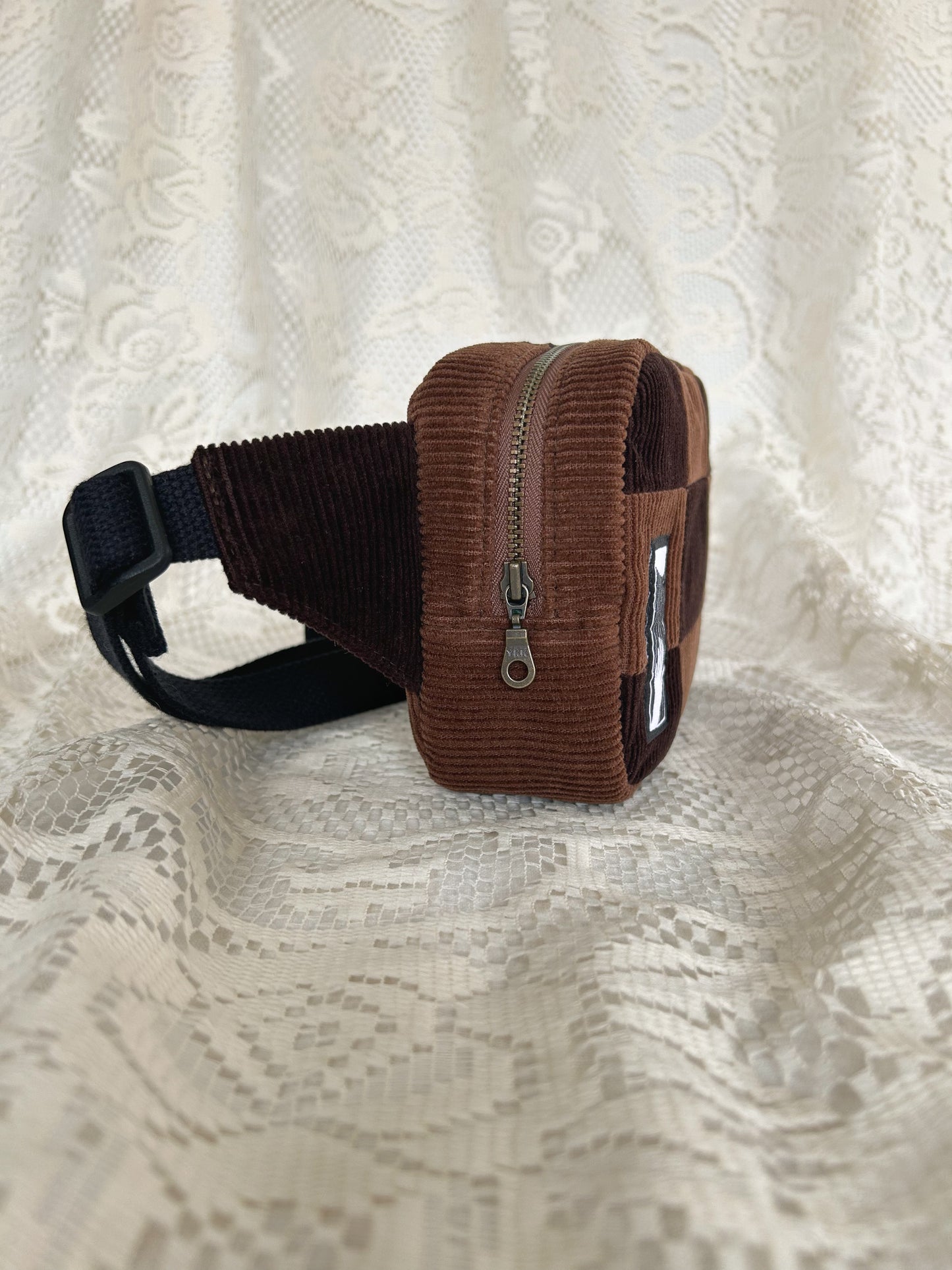 Side view of the same fanny pack showing the antique brass zipper with an ivory lace backdrop