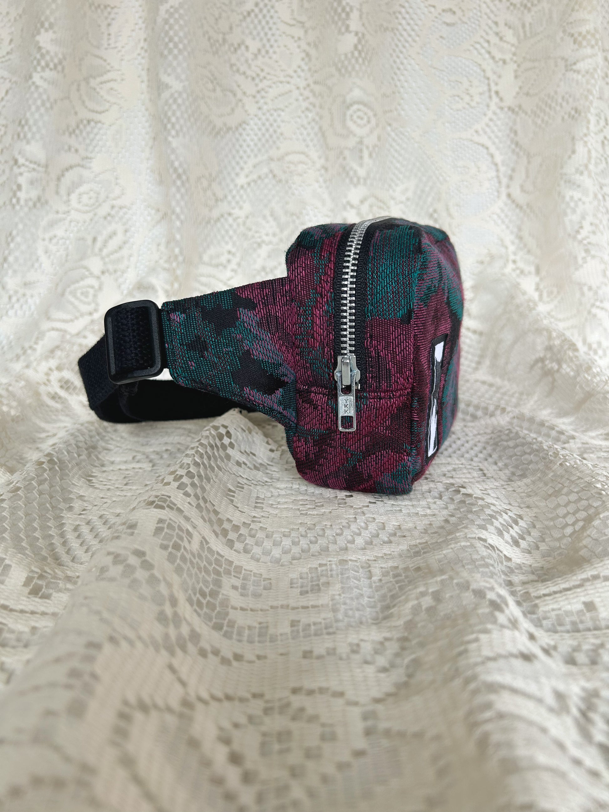 Side view of the same fanny pack showing the aluminum zipper with an ivory lace backdrop