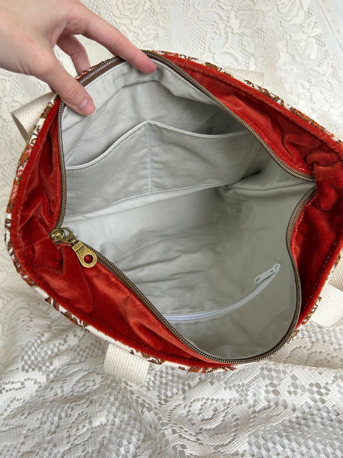 Ivory twill interior lining of the tote bag with one zippered pocket and two slip pockets with an ivory lace backdrop