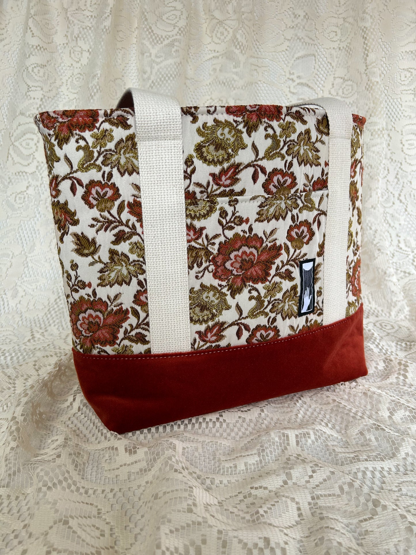Front angled view of the same tote bag on an ivory lace backdrop