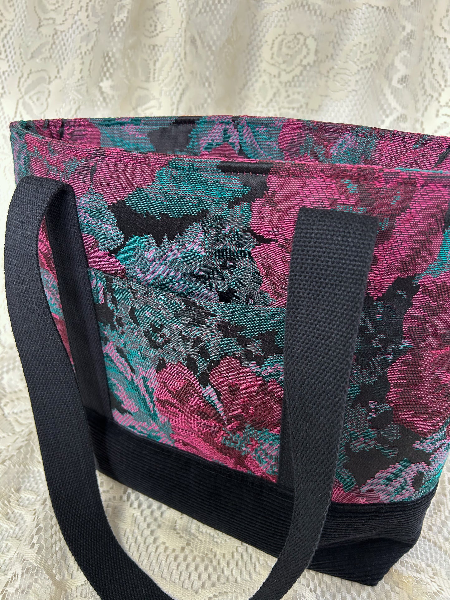 Close-up view of the same tote bag showing the exterior slide pocket with an ivory lace backdrop