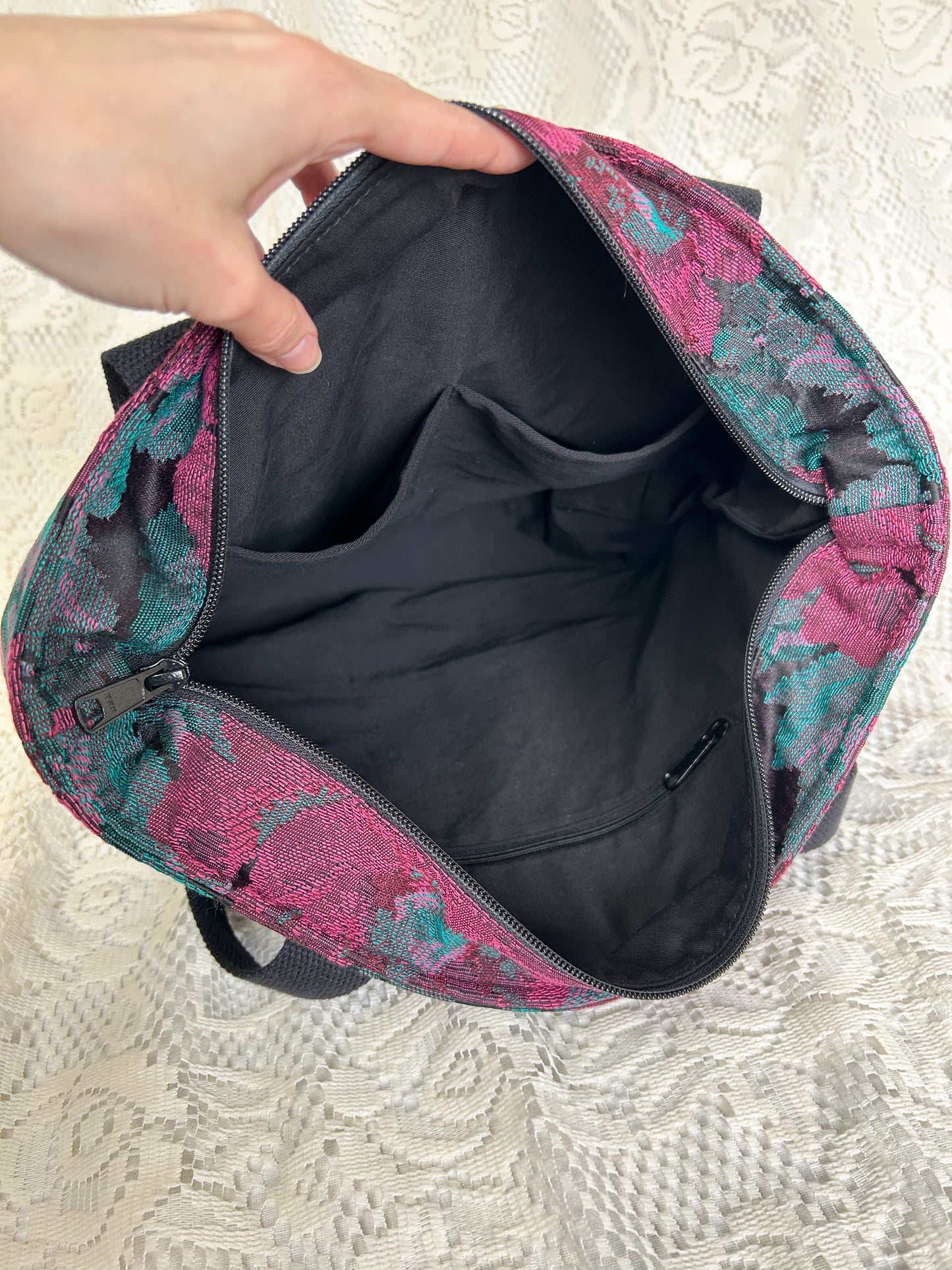Black twill interior lining of the same bag with one zippered pocket and two slip pockets with an ivory lace backdrop