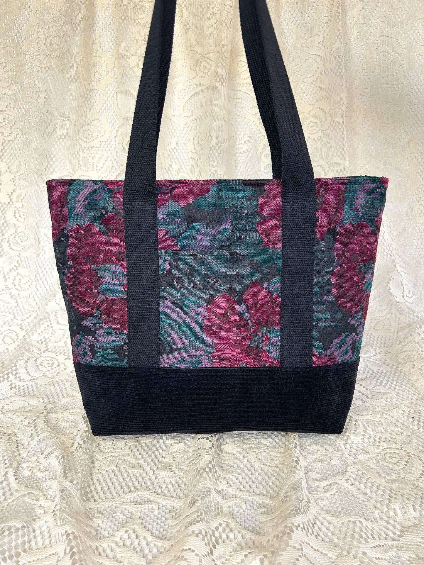Tote bag made from burgundy, turquoise, and black floral fabric and black corduroy, with black cotton webbing straps with an ivory lace backdrop