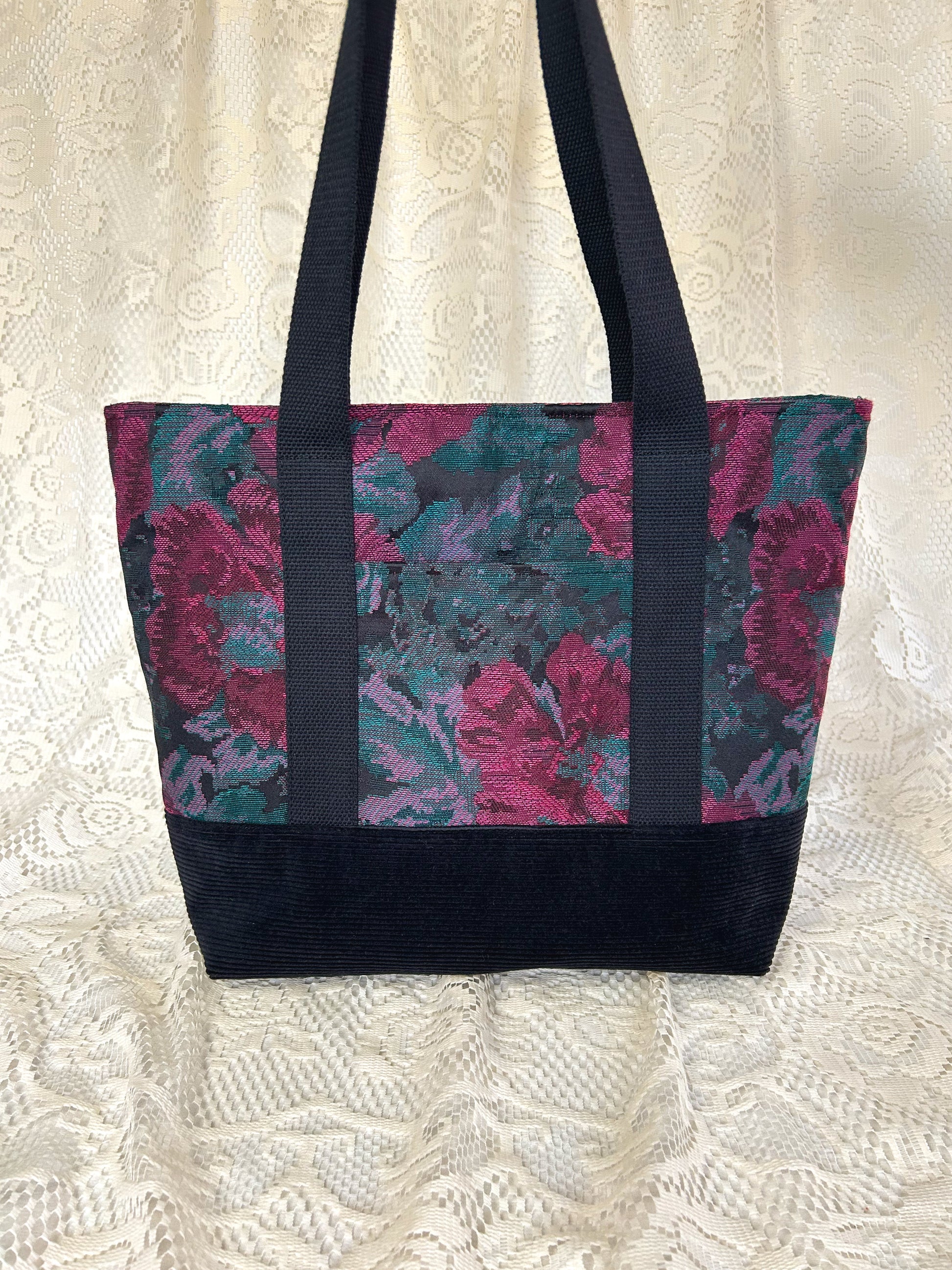 Tote bag made from burgundy, turquoise, and black floral fabric and black corduroy, with black cotton webbing straps with an ivory lace backdrop