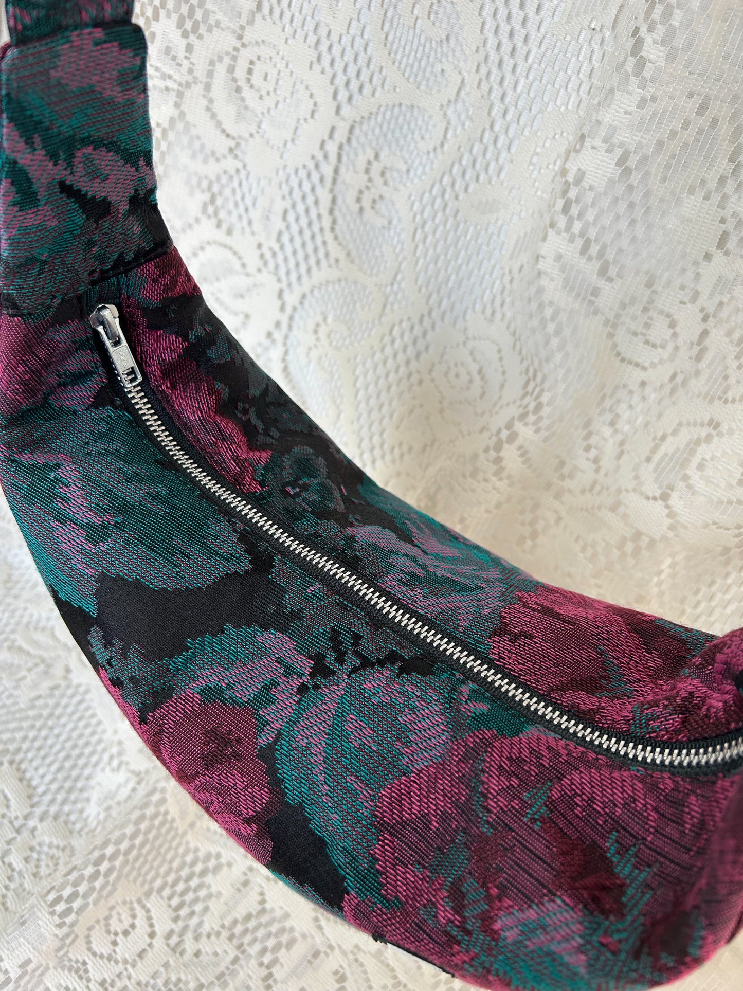Top view of the crescent moon bag showing the aluminum zipper with an ivory lace backdrop