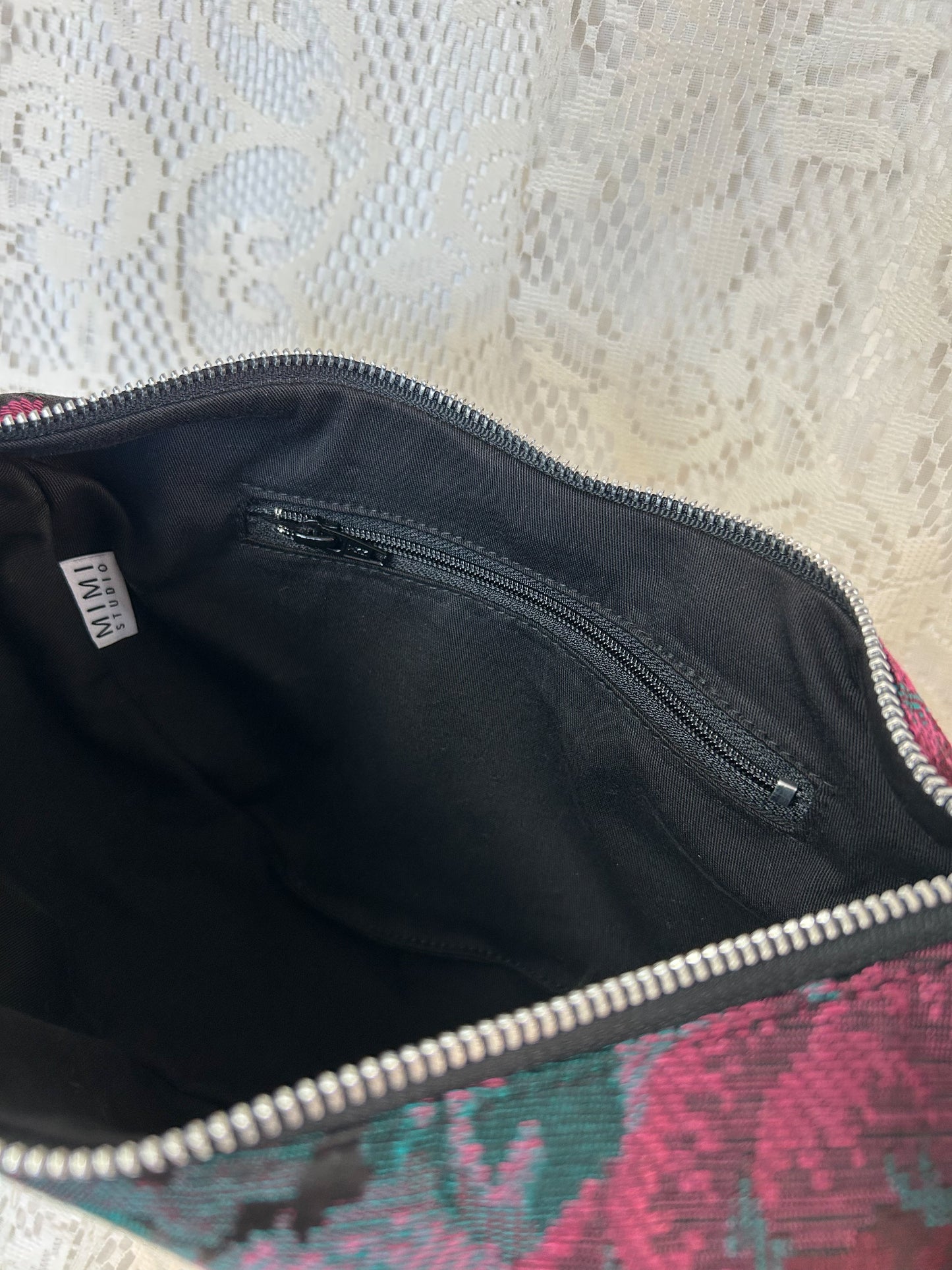 Interior lining of the crescent moon bag made from black twill fabric with a zippered pocket with an ivory lace backdrop