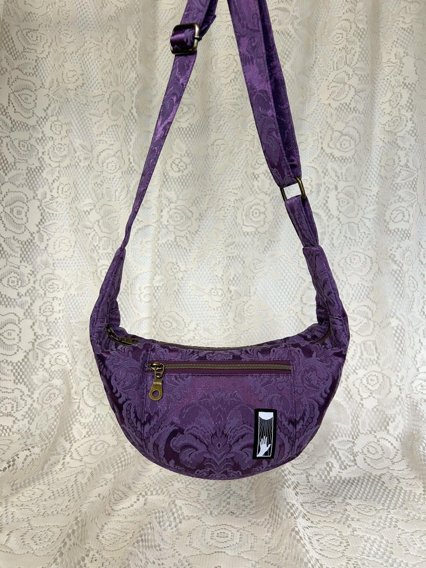 Front view of the purple damask fabric crescent moon bag with an ivory lace backdrop