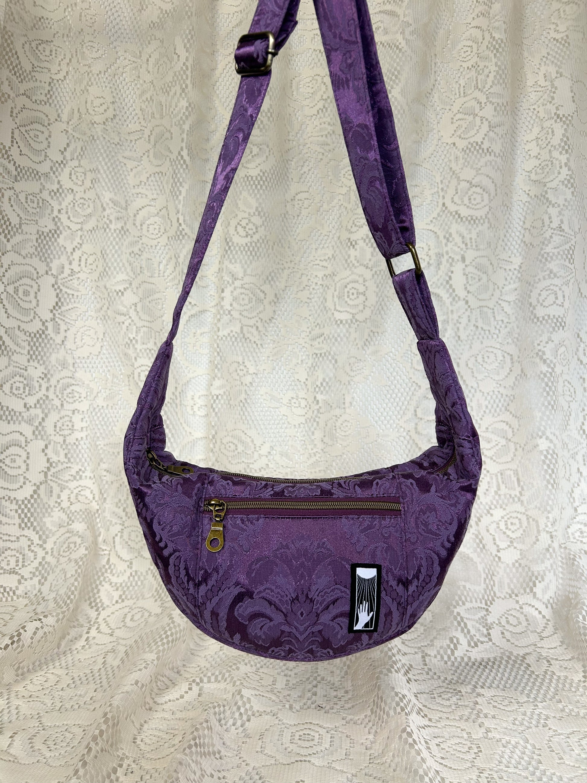 Front view of the purple damask fabric crescent moon bag with an ivory lace backdrop