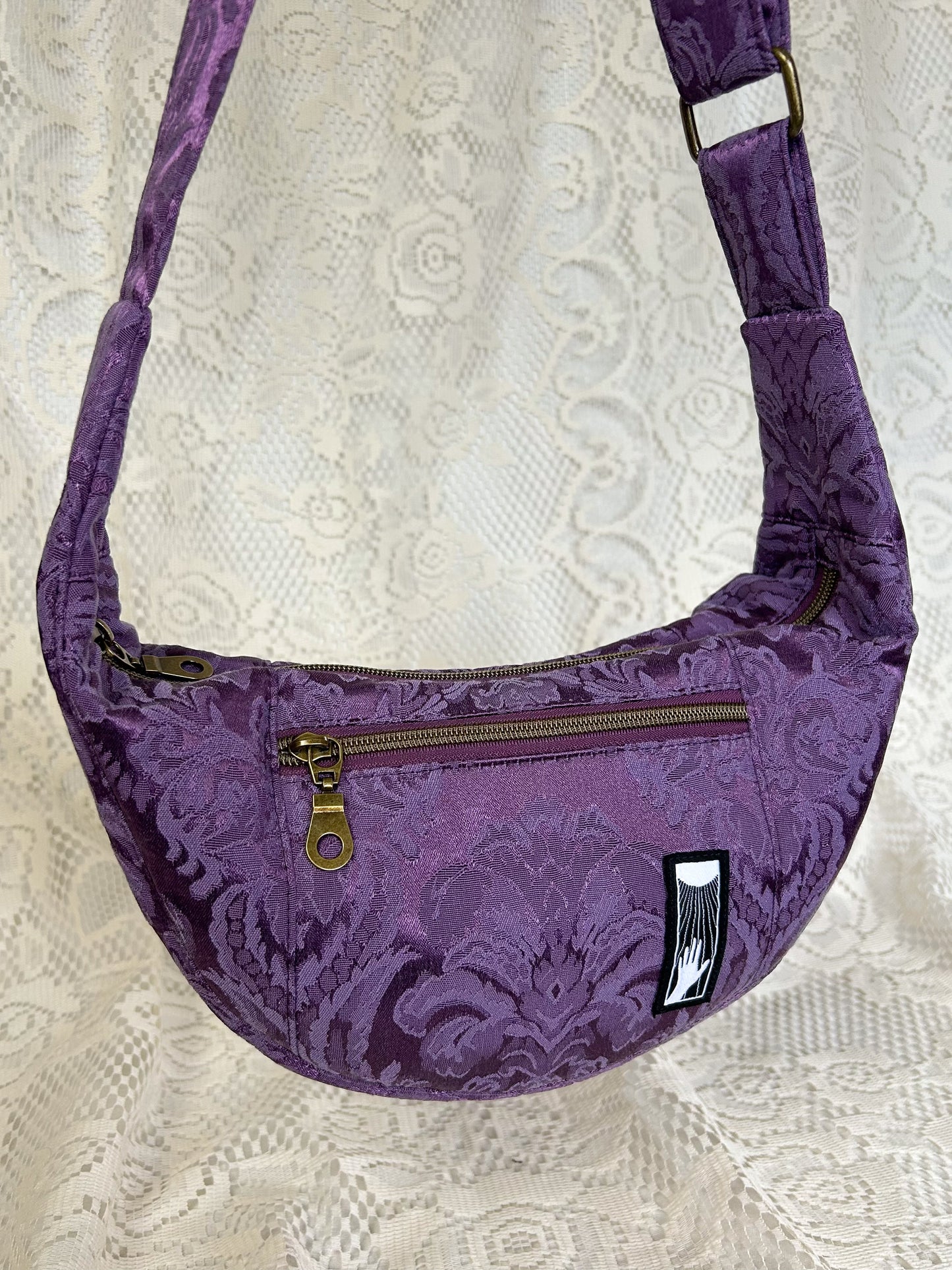 Close up view of the crescent moon bag showing the front zippered pocket in front of an ivory lace backdrop