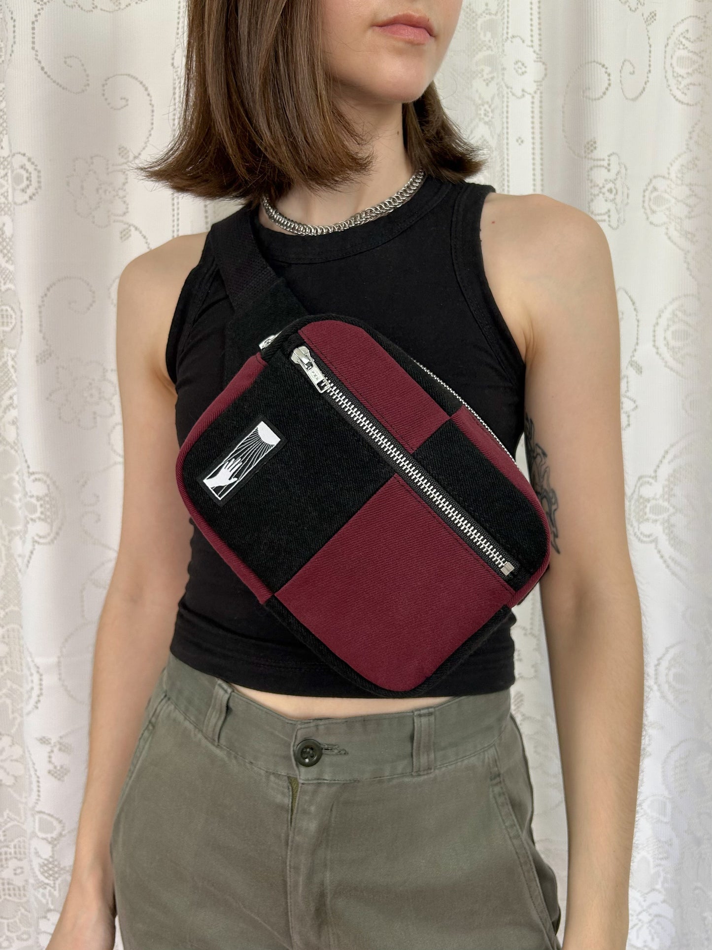 Woman wearing the half black, half burgundy denim colour block fanny pack cross-body in front of a white lace backdrop