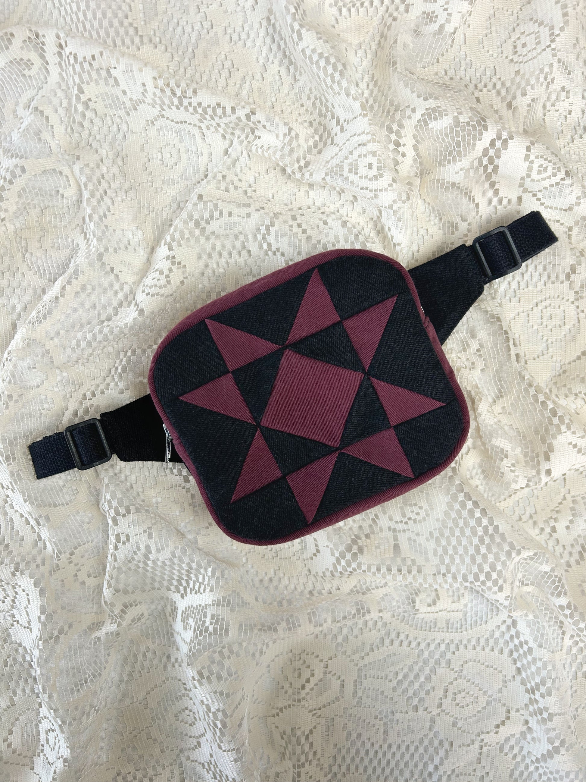 Flat lay view of a fanny pack with a star pattern made from patches of burgundy and black denim on an ivory lace background