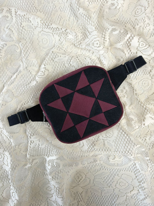 Flat lay view of a fanny pack with a star pattern made from patches of burgundy and black denim on an ivory lace background