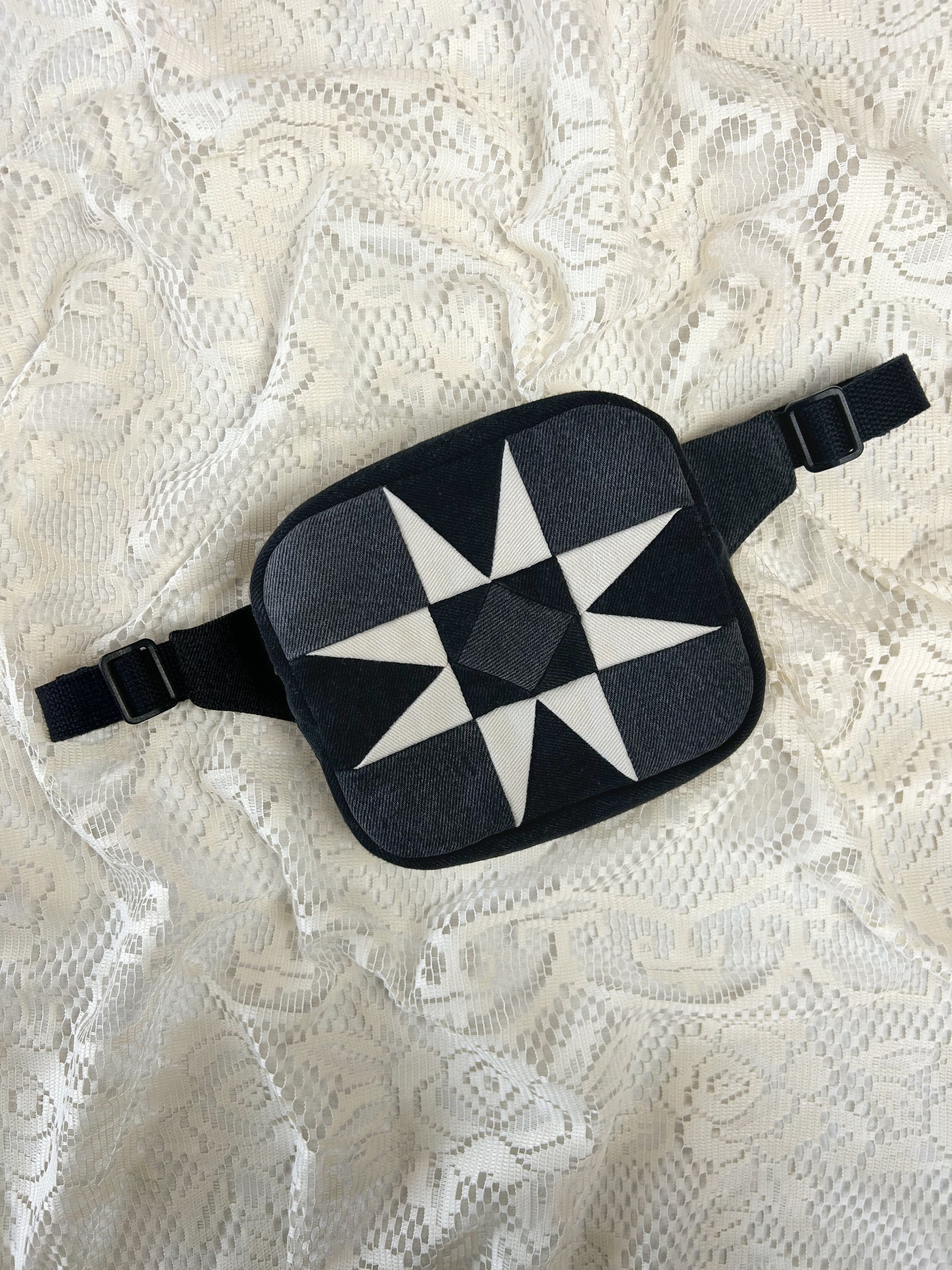 Flat lay view of a fanny pack with a star pattern made using ivory, black and grey denim patches on an ivory lace background