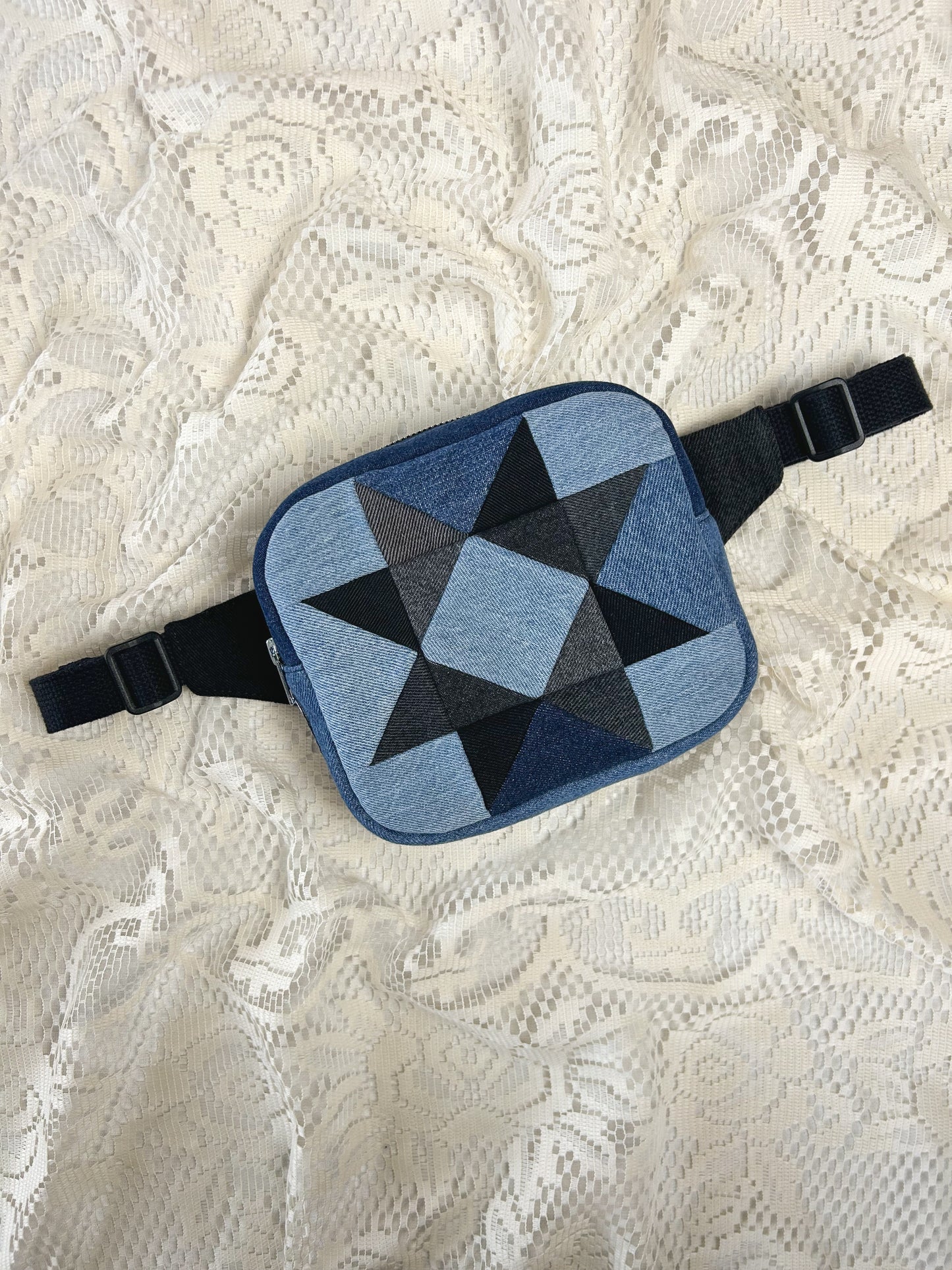 Flat lay view of a fanny pack with a patchwork star pattern made from blue, grey and black denim patches on an ivory lace background