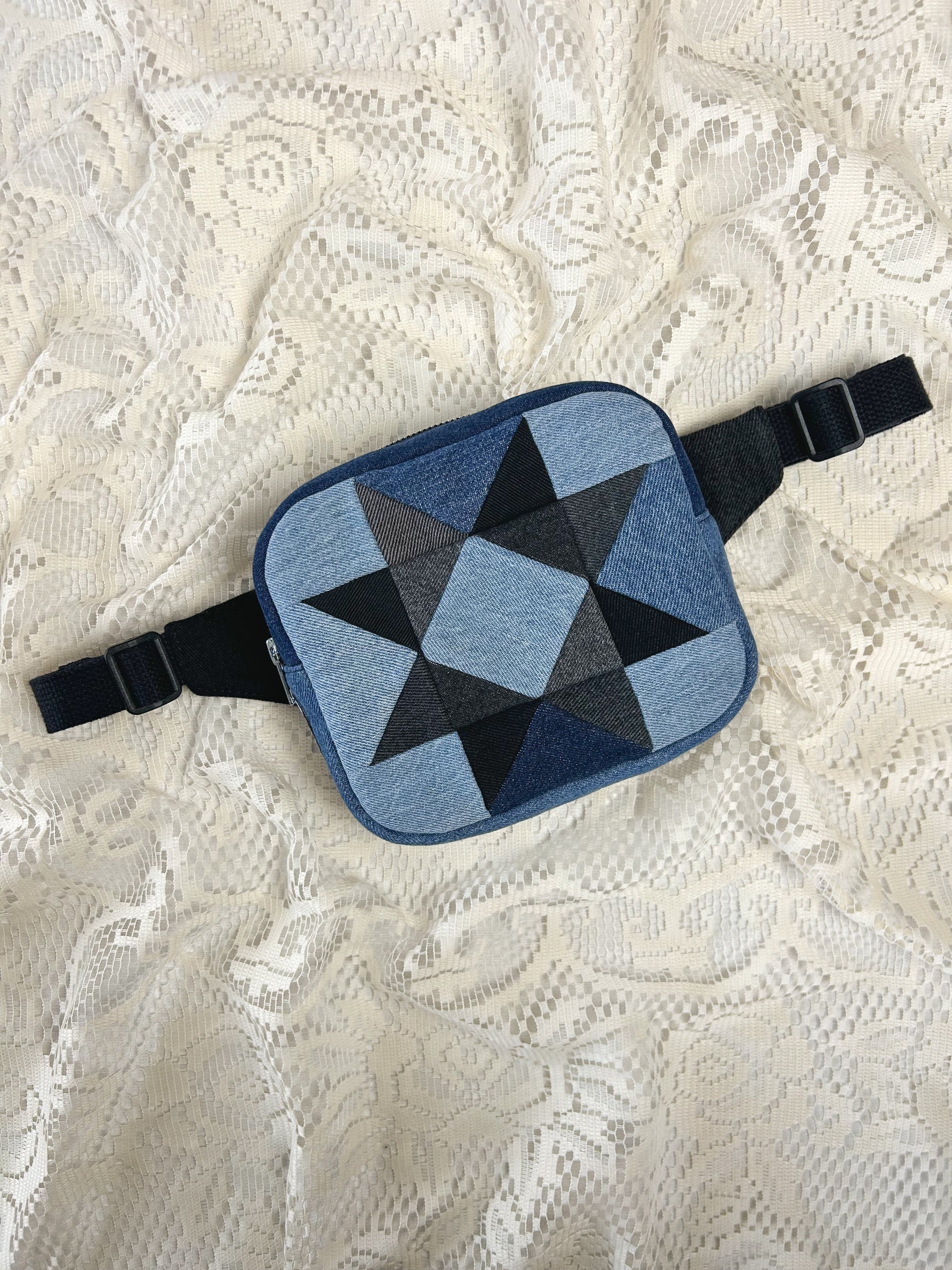 Flat lay view of a fanny pack with a patchwork star pattern made from blue, grey and black denim patches on an ivory lace background