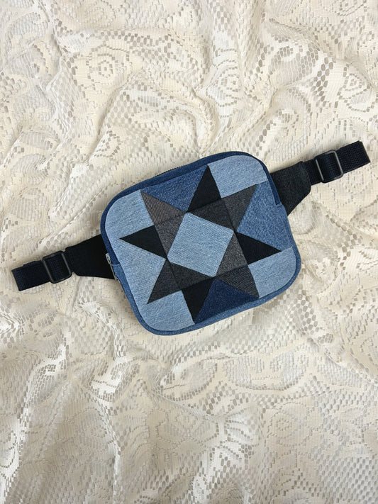 Flat lay view of a fanny pack with a patchwork star pattern made from blue, grey and black denim patches on an ivory lace background