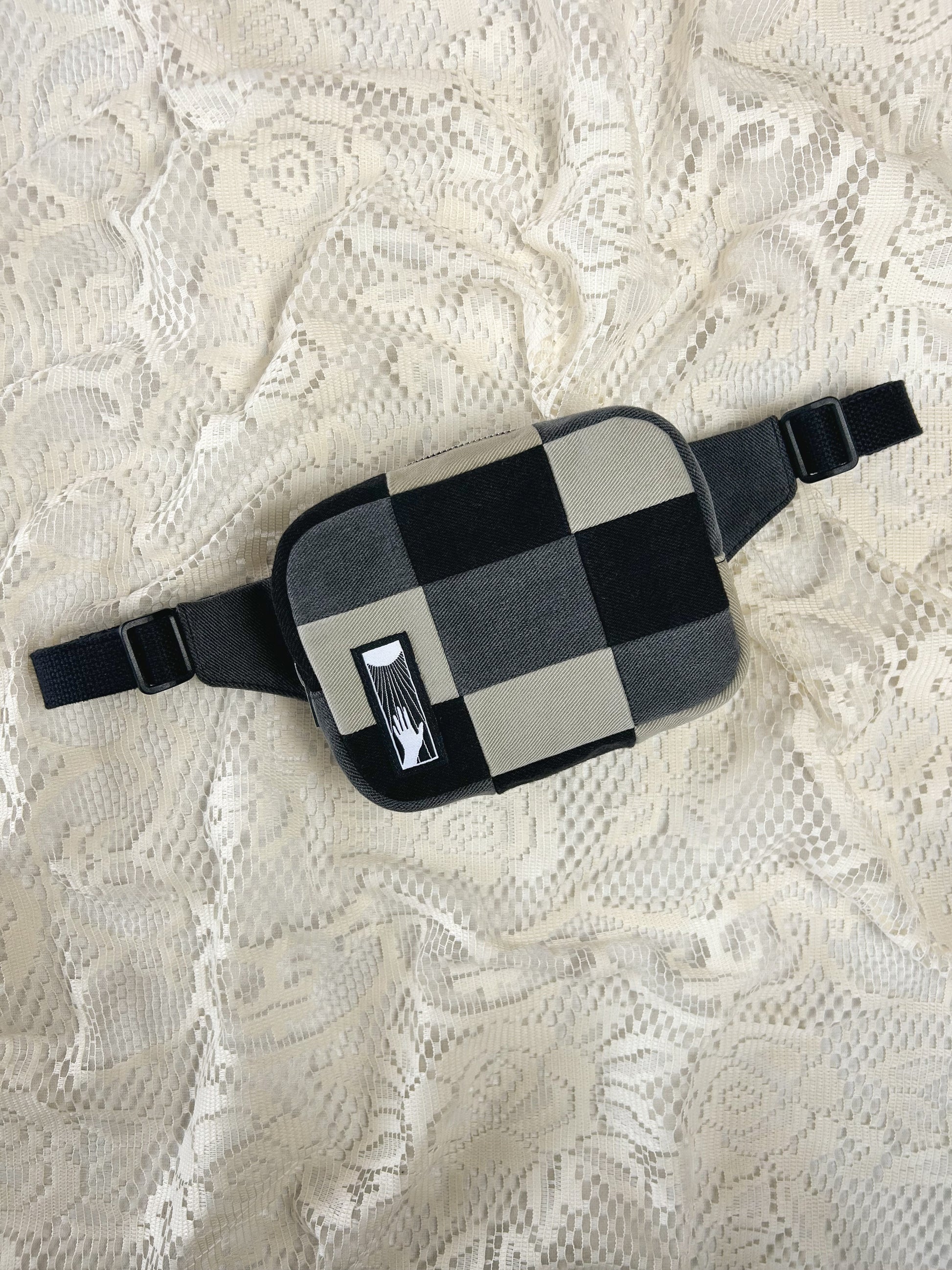 Flat lay view of a fanny pack with grey, black and ivory patches on an ivory lace background