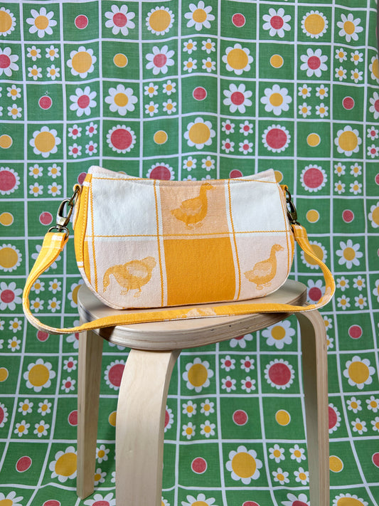 Light orange and white checkered duck patterned handbag on a wooden stool in front of a floral backdrop