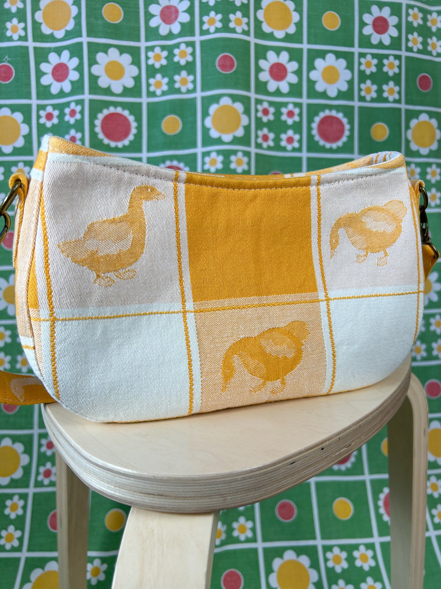 Closeup of the back side of the same handbag on a wooden stool in front of a floral backdrop