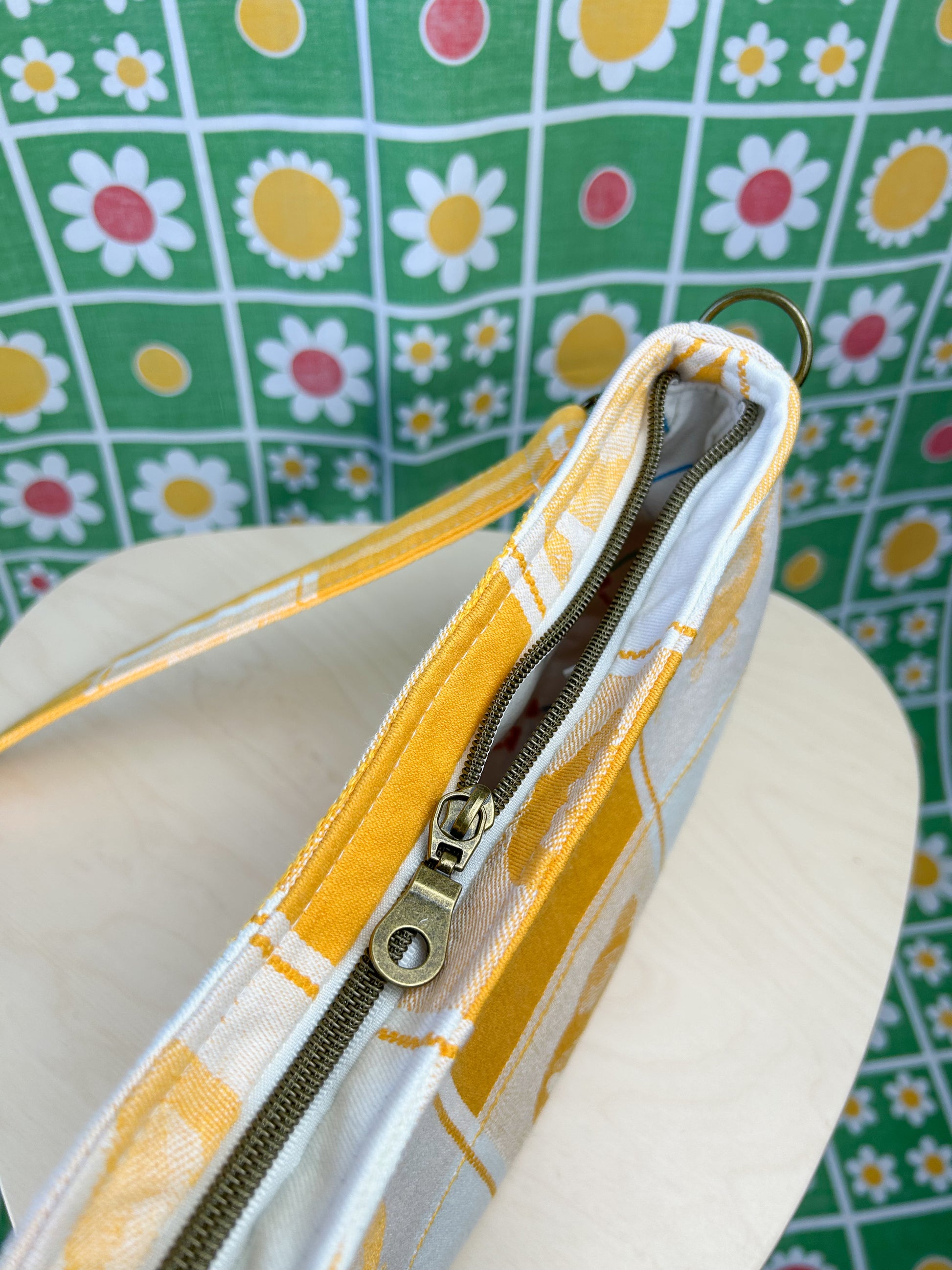 Top view of the same handbag showing the nylon antique brass exterior zipper on a wooden stool in front of a floral backdrop