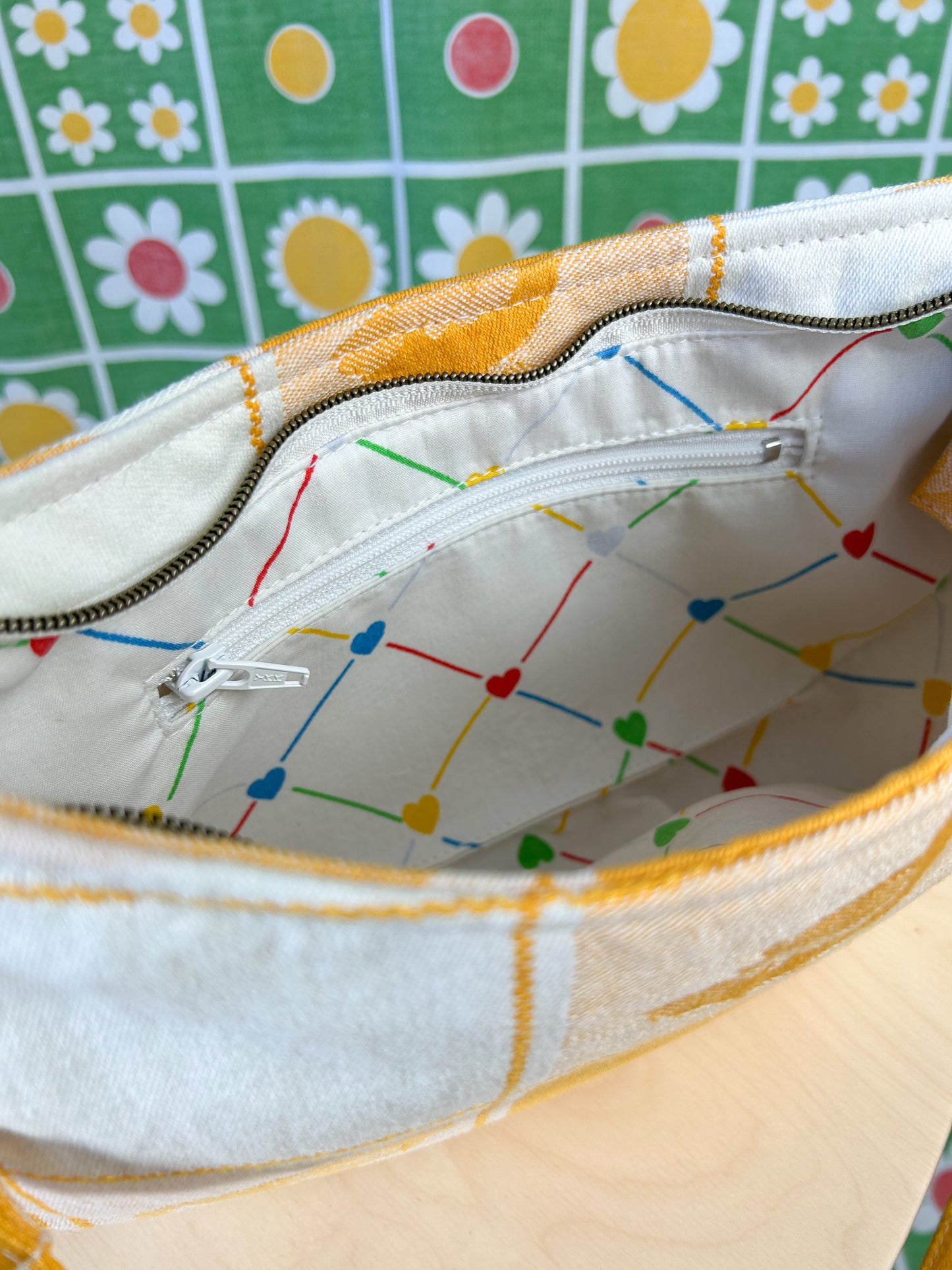 Interior view of the same handbag showing the heart patterned lining and zippered pocket on a wooden stool in front of a floral backdrop
