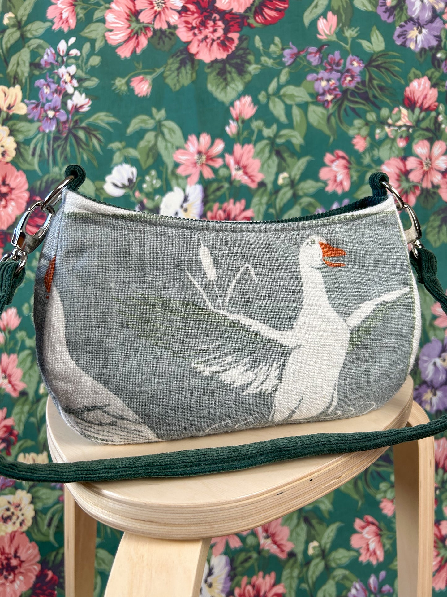 Handbag with a white duck print and  on a wooden stool against a floral background