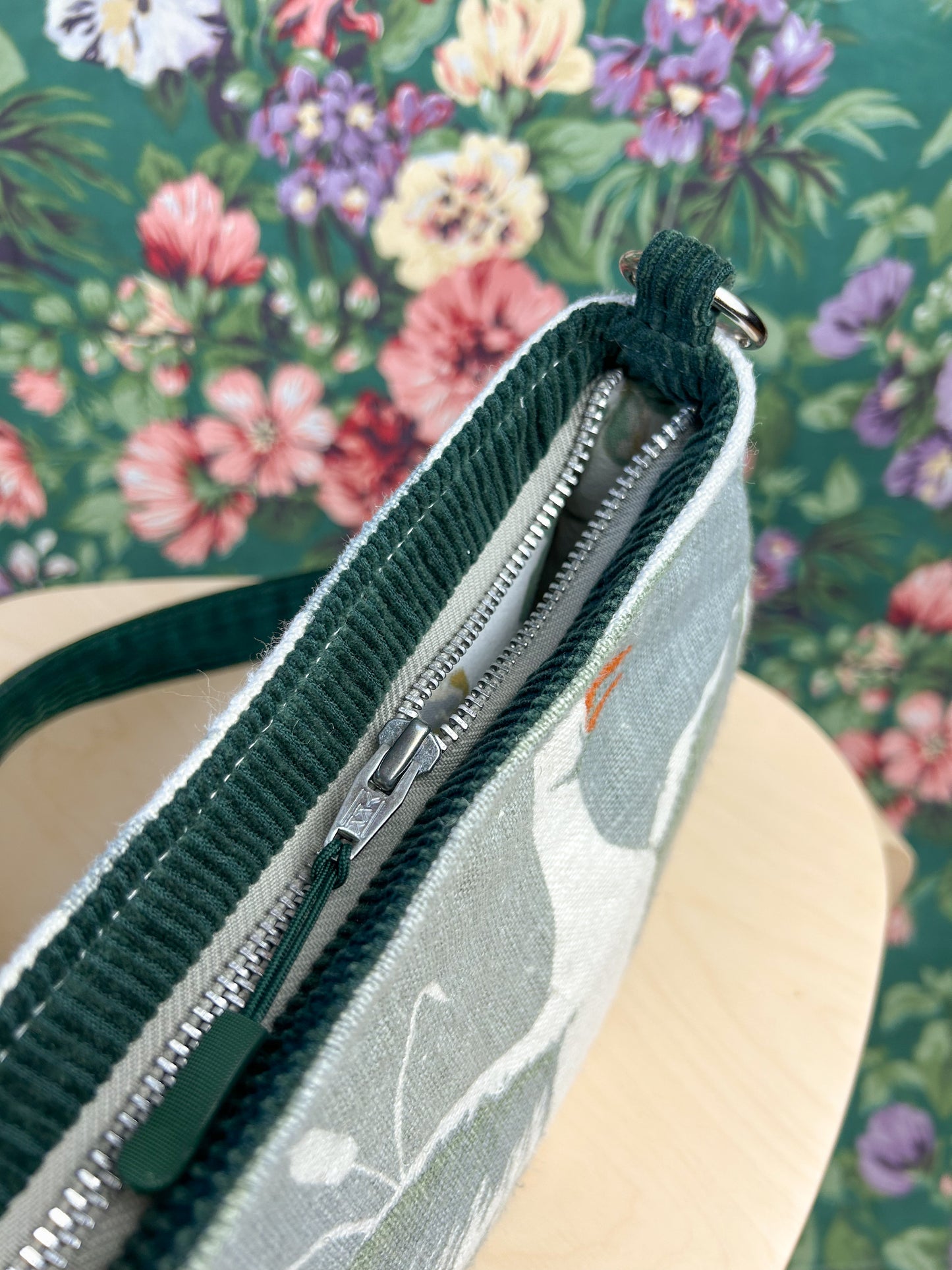 Top view of the bag showing the exterior zipper on a wooden stool in front of a floral backdrop