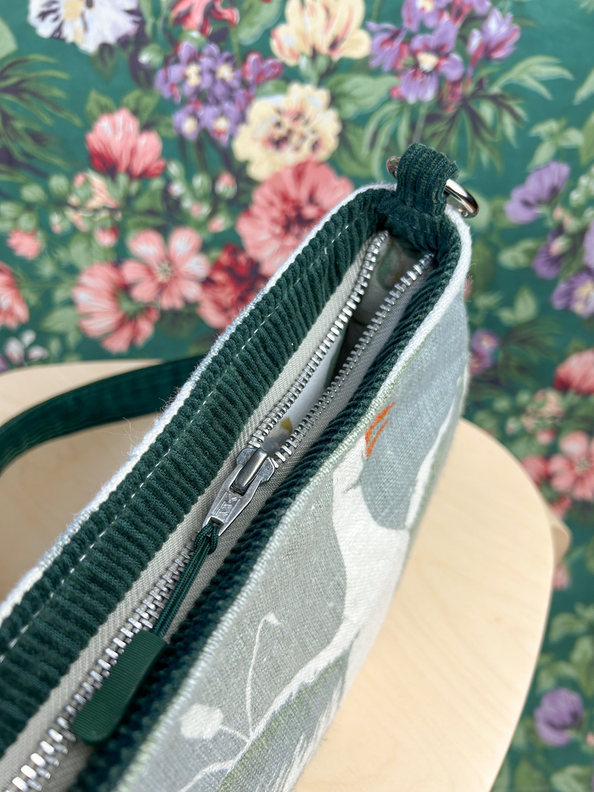 Top view of the bag showing the exterior zipper on a wooden stool in front of a floral backdrop