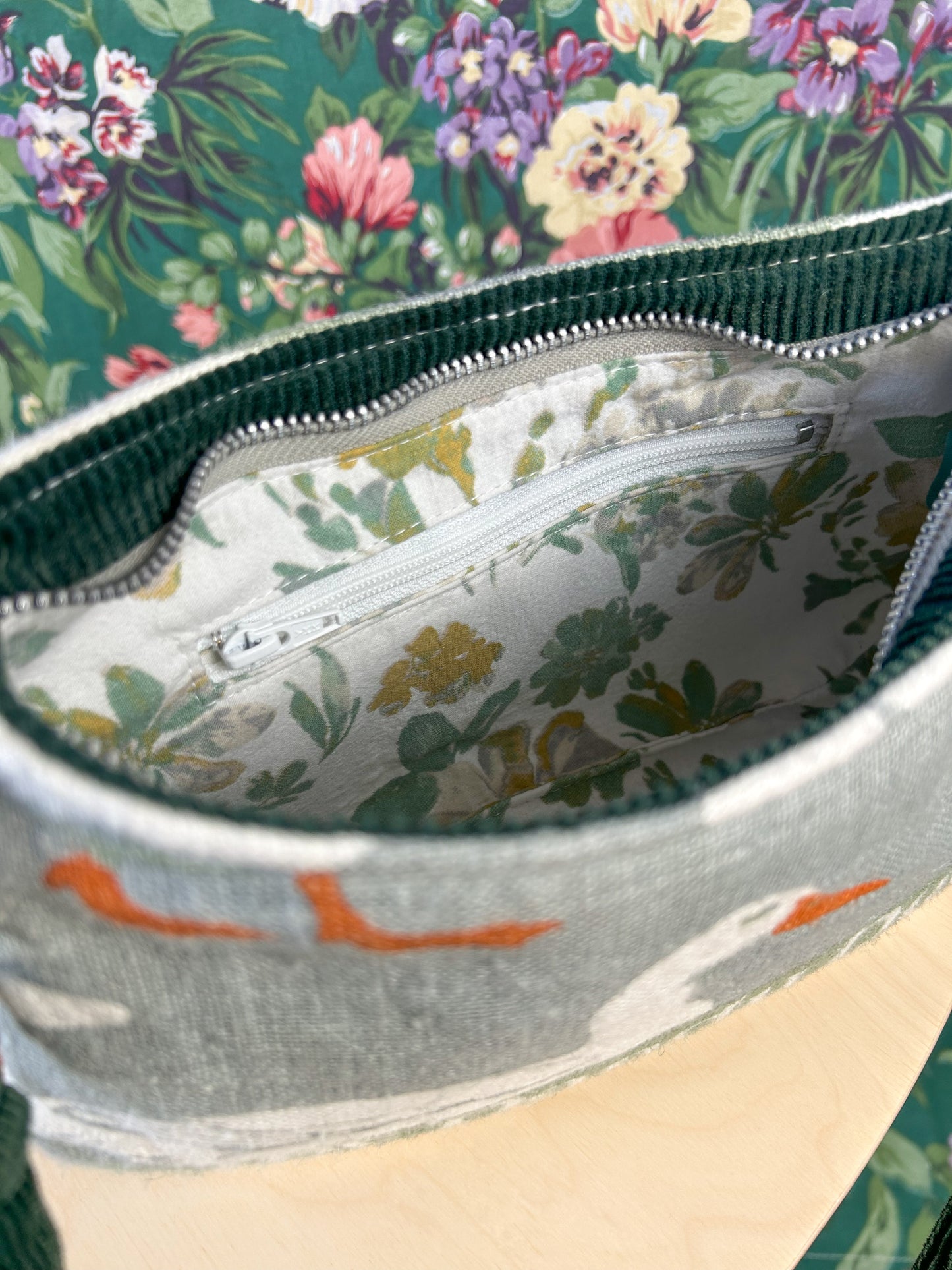 Interior view of the bag showing the floral lining and zippered pocket on a wooden stool in front of a floral backdrop