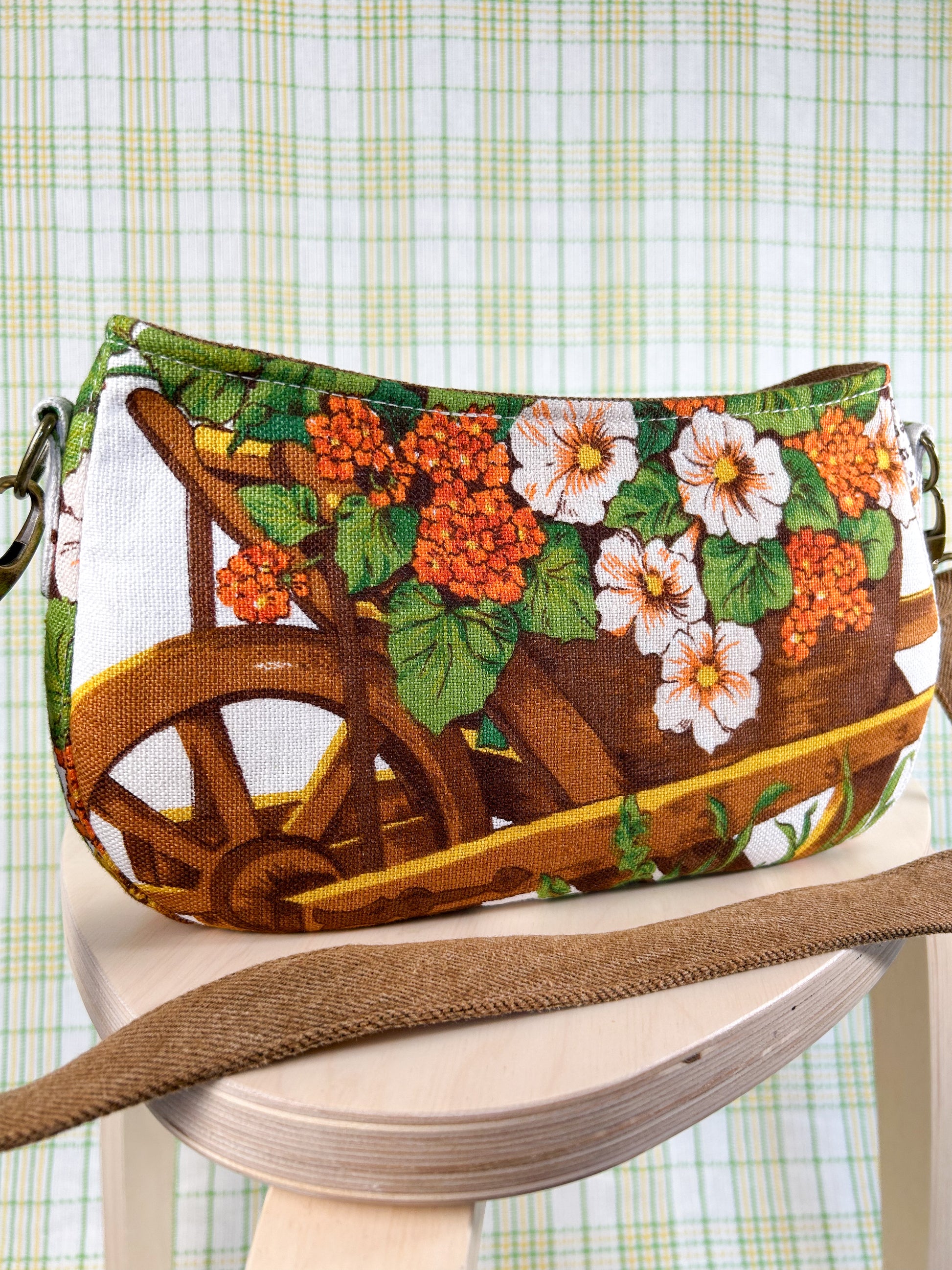 Handbag with a wheelbarrow and flower design on a wooden stool in front of a plaid backdrop