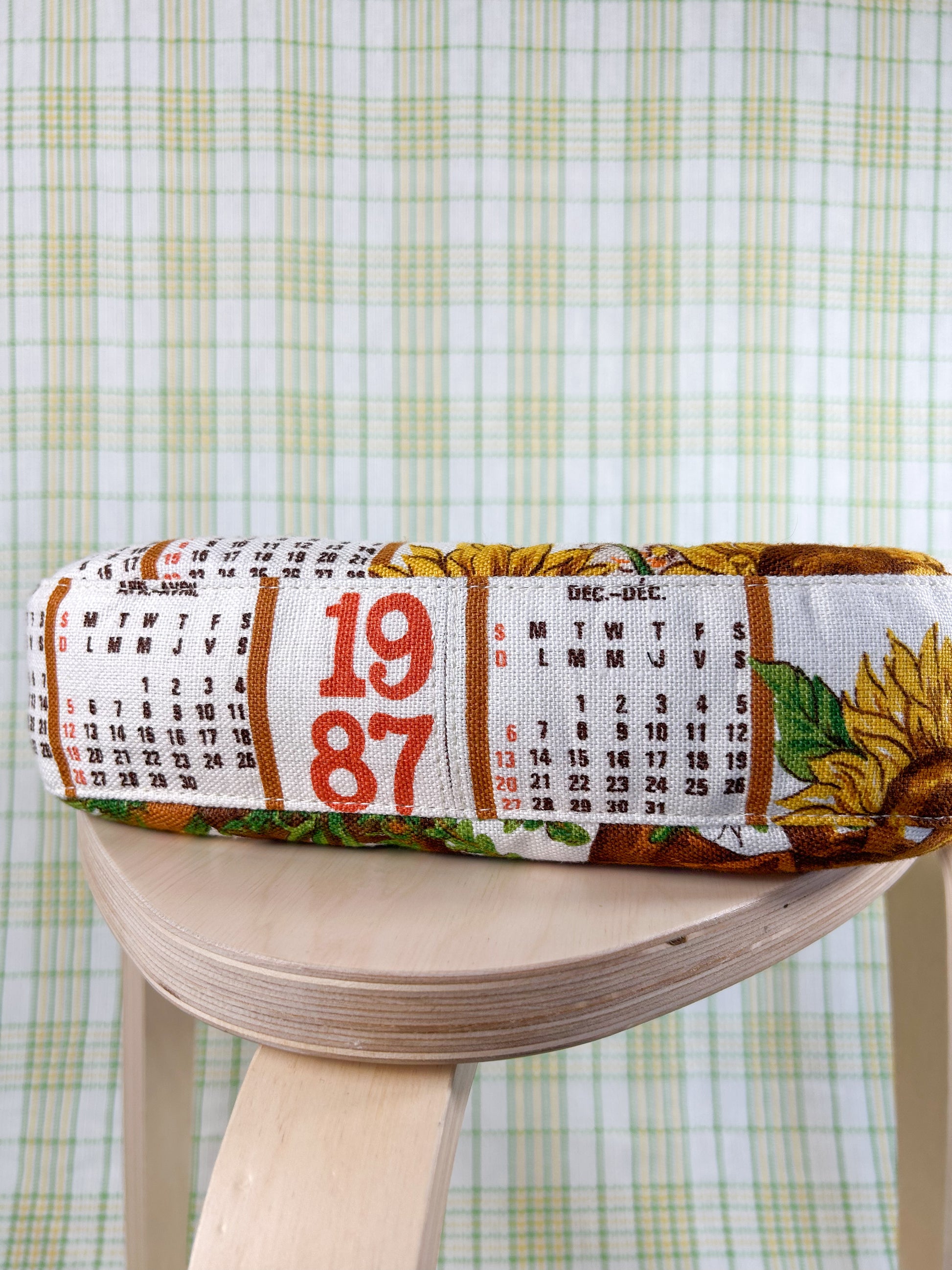 Bottom of the handbag with a 1987 calendar print on a wooden stool in front of a plaid backdrop