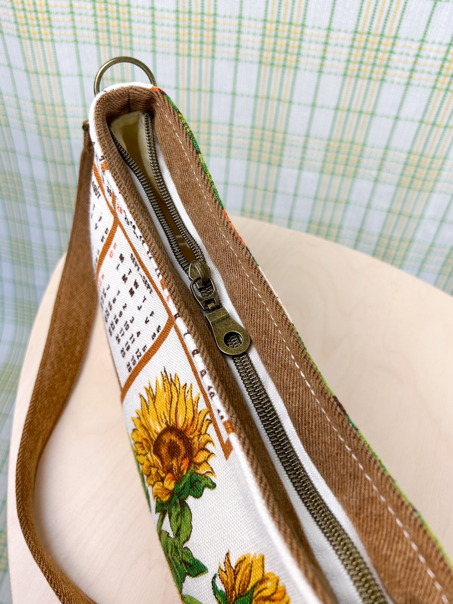 Top view of the handbag showing the antique brass nylon zipper on a wooden stool with a plaid backdrop